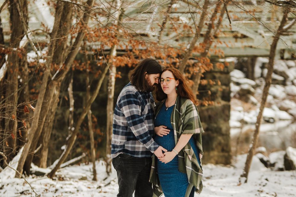 A couple shares an intimate moment in a snowy winter forest setting while wearing casual outdoor clothing.