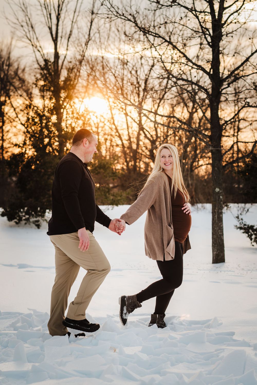 A sequence of four photos showing a couple playfully falling into deep snow at sunset with bare winter trees in background.