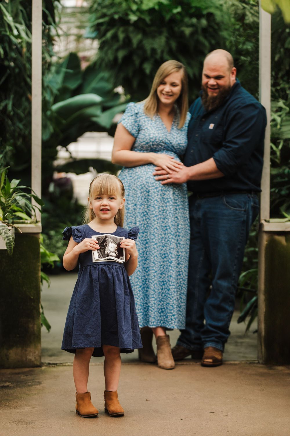 A family in coordinated blue outfits poses together in a garden setting for a series of candid outdoor portraits.