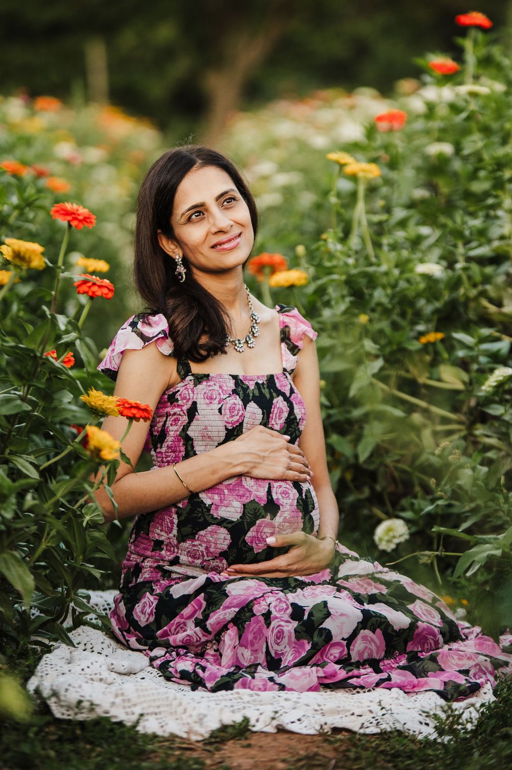 A floral dress stands out against vibrant orange and yellow zinnias in a lush garden setting.