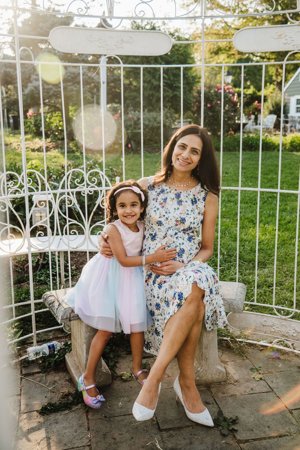 A floral dress and tulle dress are worn while sitting on decorative white garden furniture outdoors on a sunny day.