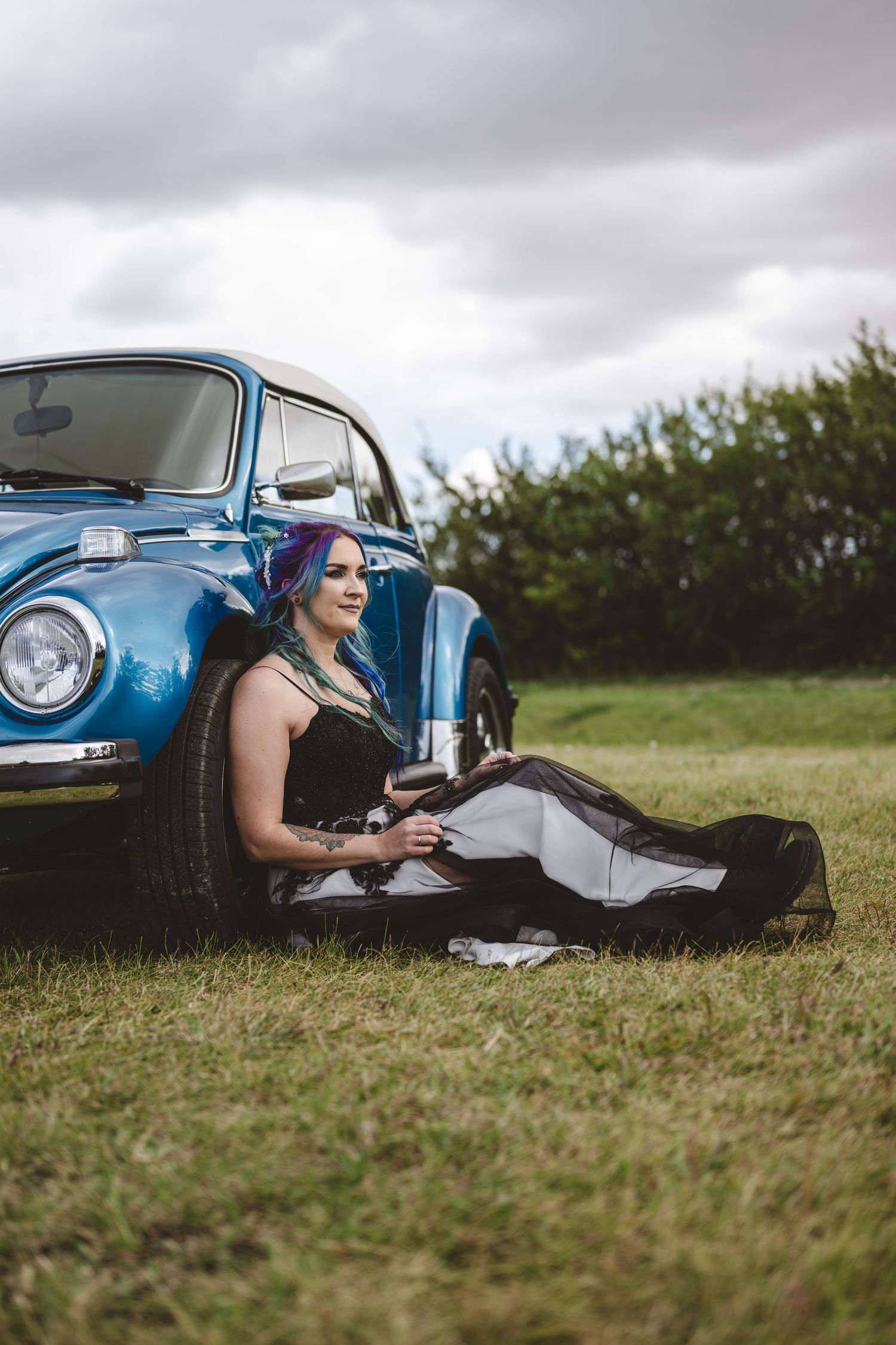 Classic blue Volkswagen Beetle parked in grassy field under cloudy sky.