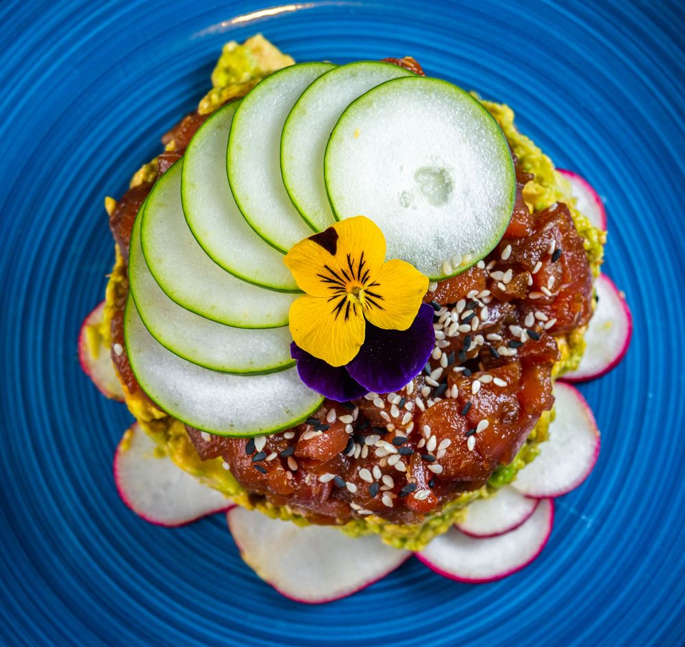 Step-by-step assembly of an open-faced sandwich with avocado, cucumber, radish slices and garnishes on a blue plate.