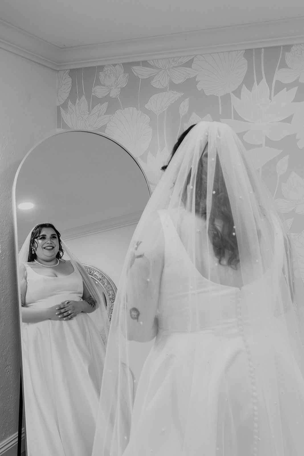 A black and white photo showing a bride in a white wedding dress and veil against a light background at River Garden Weddings and Events.