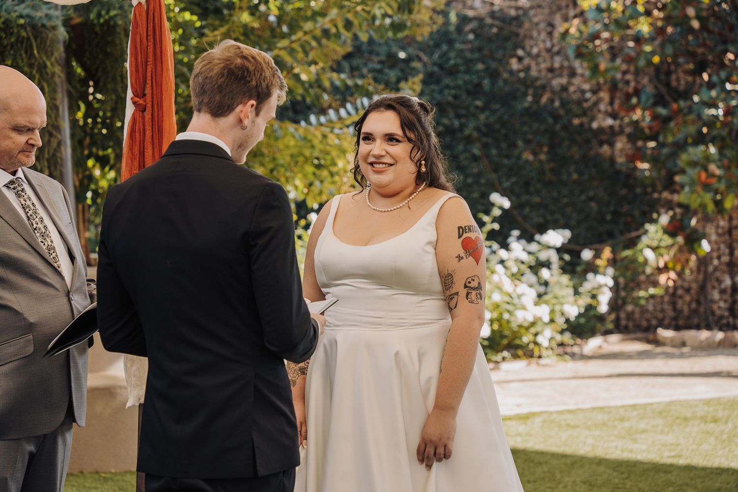 A couple exchanges vows on their wedding day in a garden setting surrounded by foliage and sunlight at River Garden Weddings and Events.