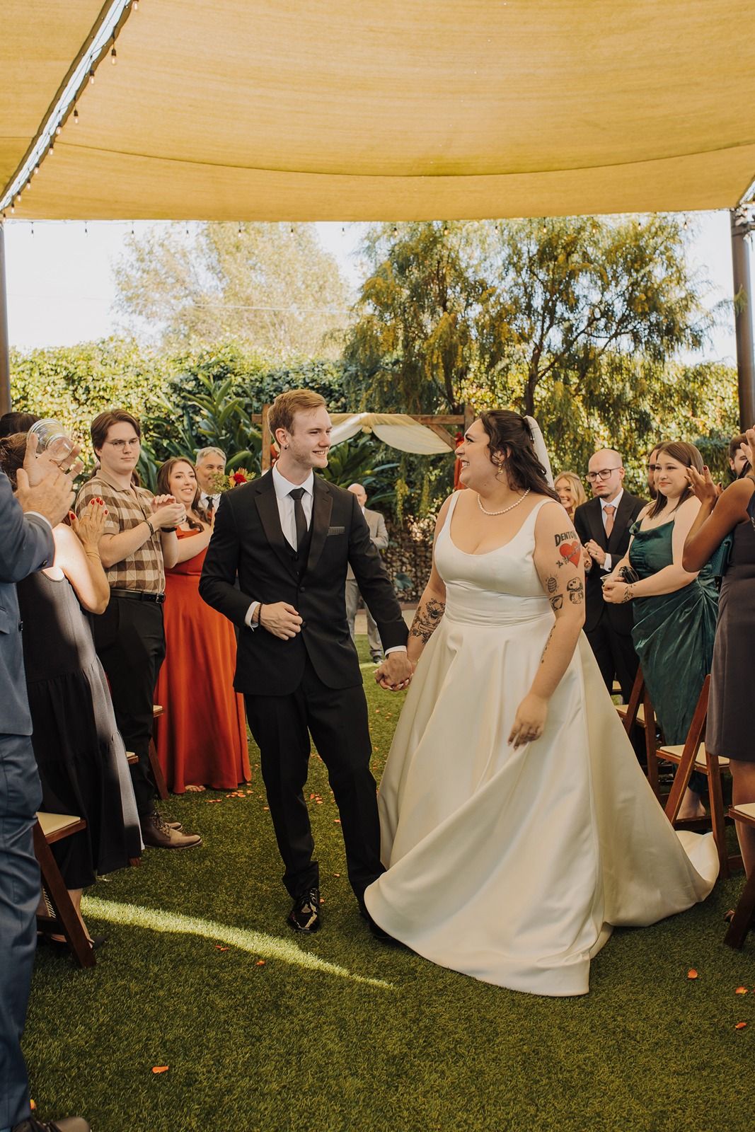 Wedding guests celebrate and cheer under a canopy tent on a sunny outdoor lawn during a reception at River Garden Weddings and Events..