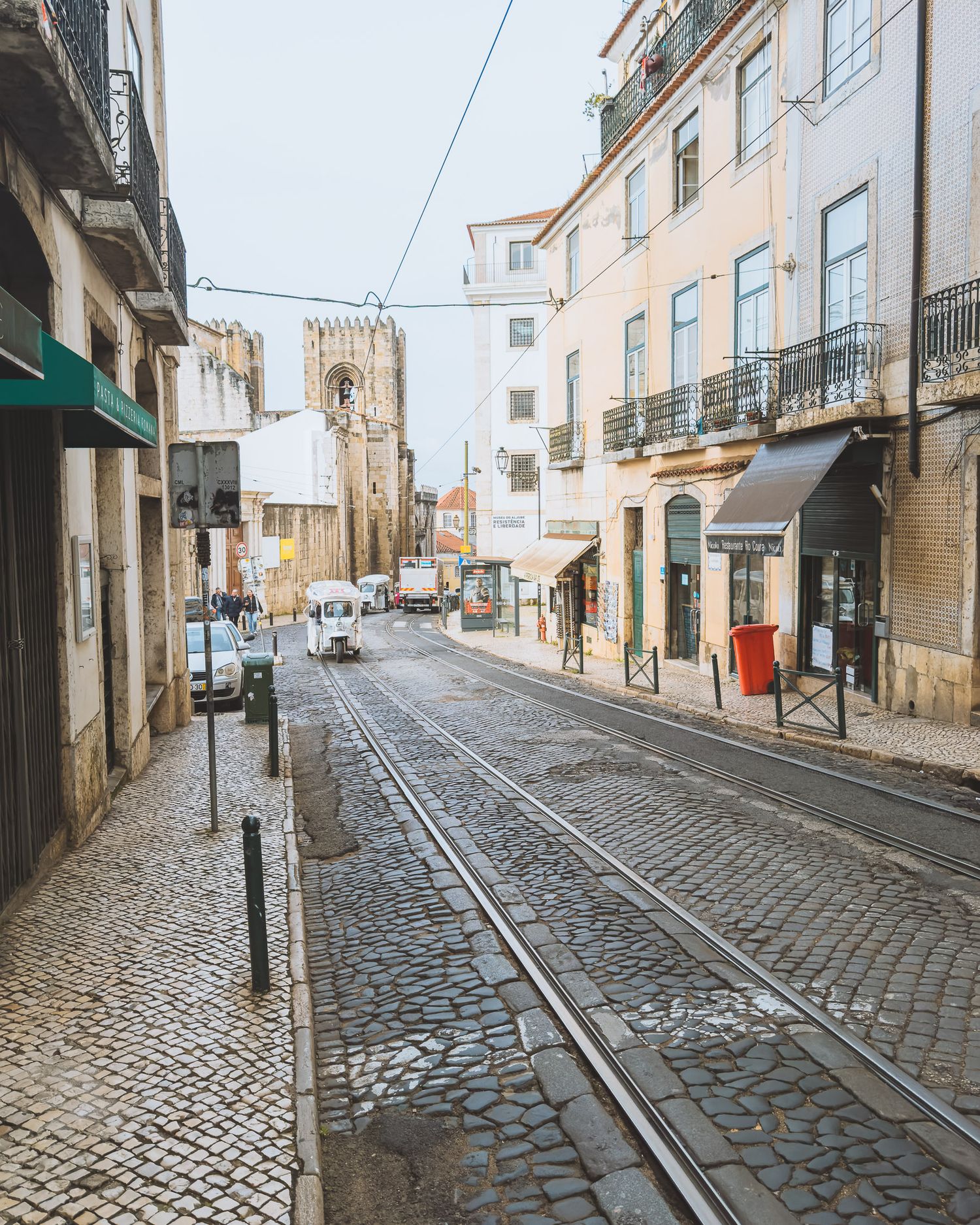 Narrow cobblestone street winding uphill between traditional Portuguese buildings with overhead power lines.