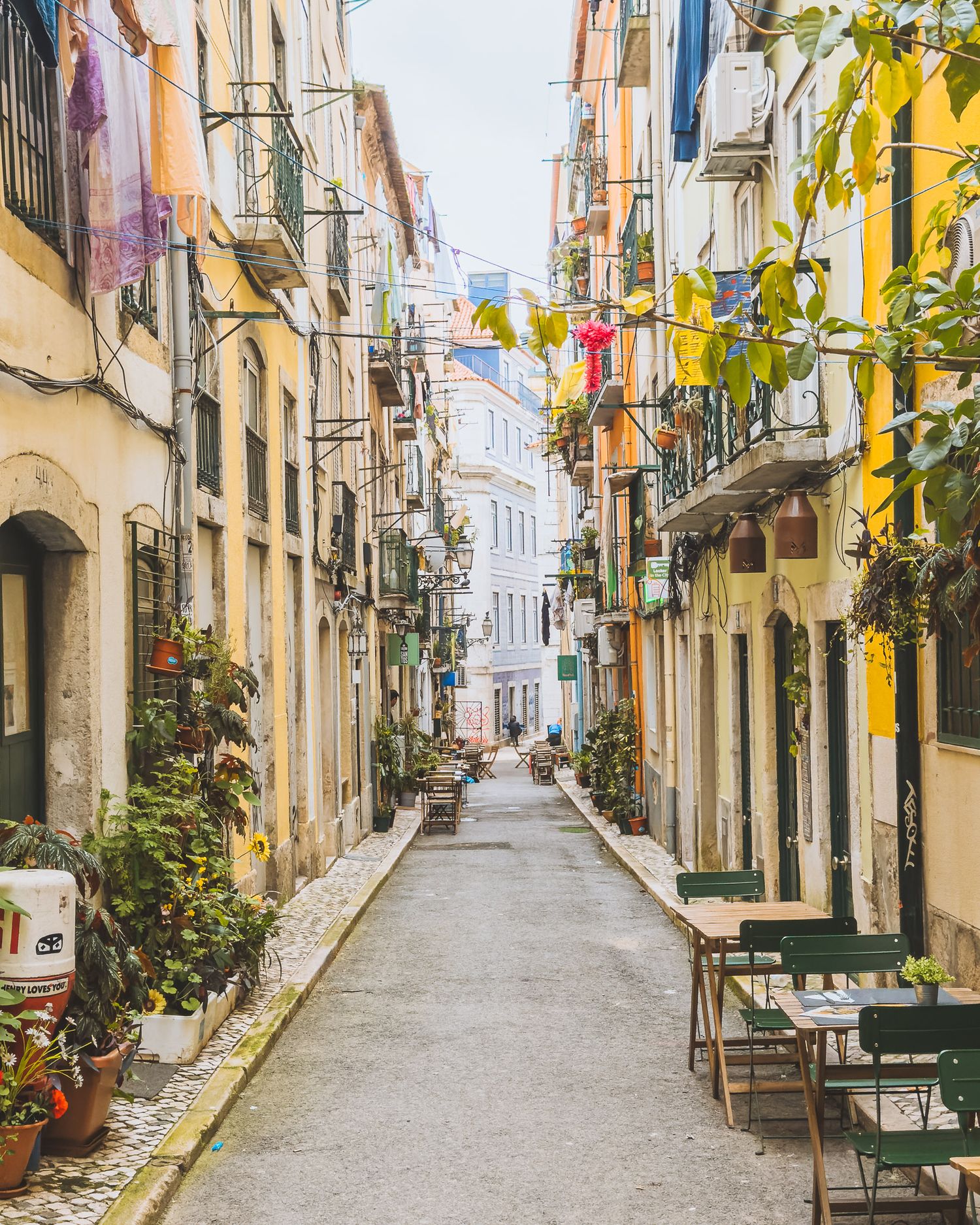 Charming narrow street lined with colorful buildings and potted plants in Lisbon's historic district.