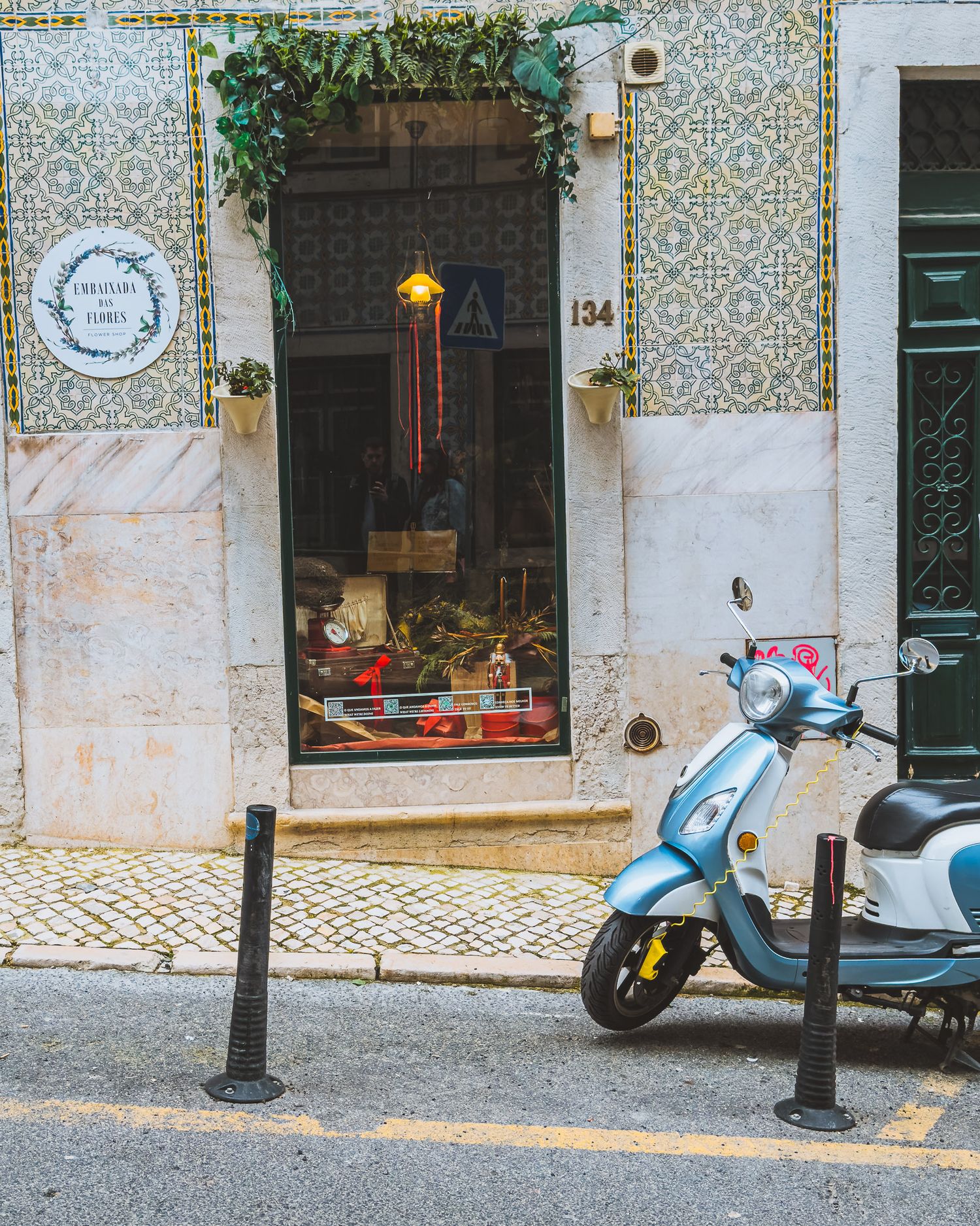 Traditional Portuguese tile-decorated storefront with parked scooters on a cobblestone street.