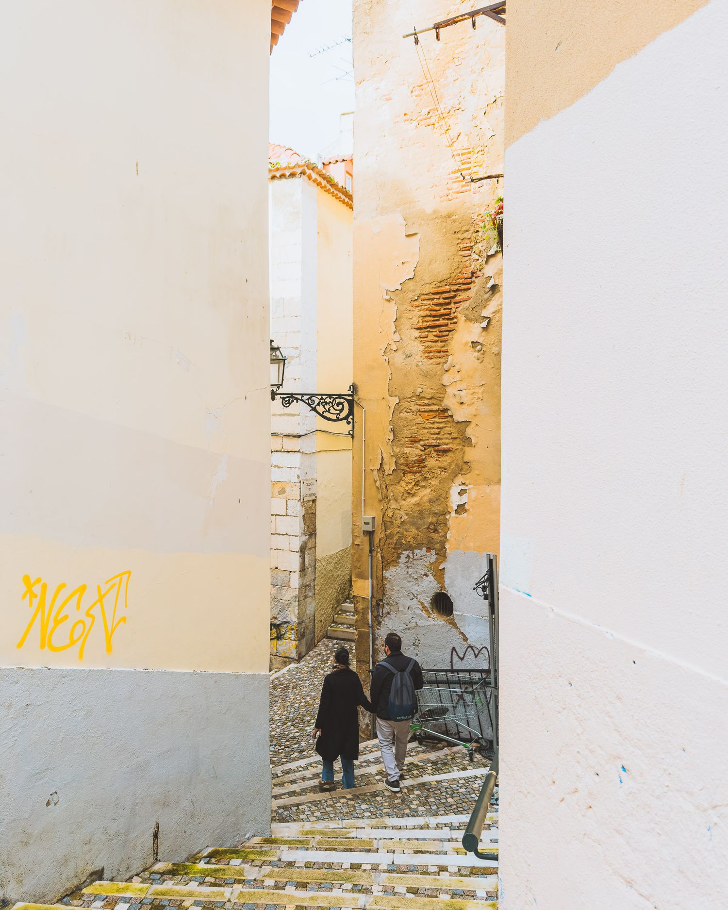 Urban street scene with white and yellow walls featuring graffiti and stone steps.