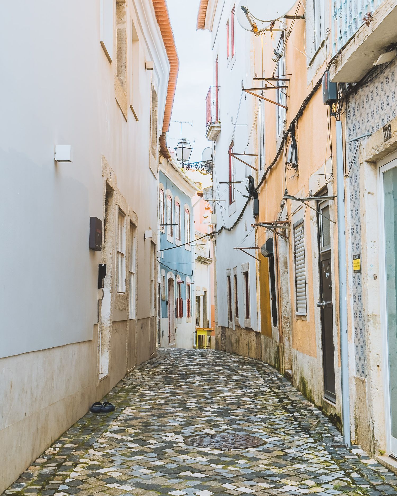 Narrow cobblestone alley with white and pastel colored buildings in a traditional European neighborhood.