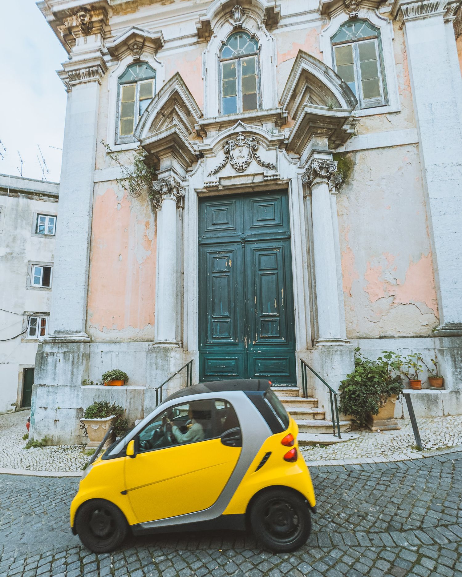 Yellow Smart car parked in front of ornate church entrance with green door and classical architecture.