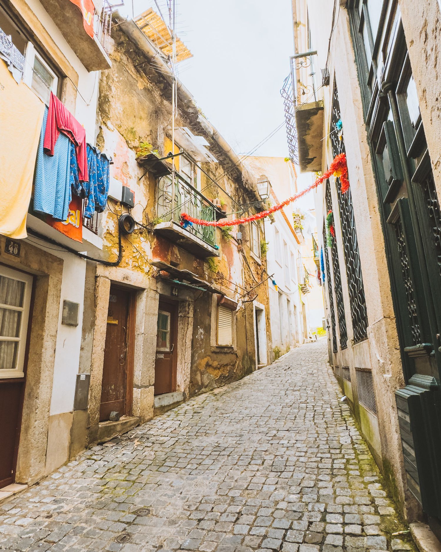 Narrow cobblestone street with colorful laundry hanging between old buildings.