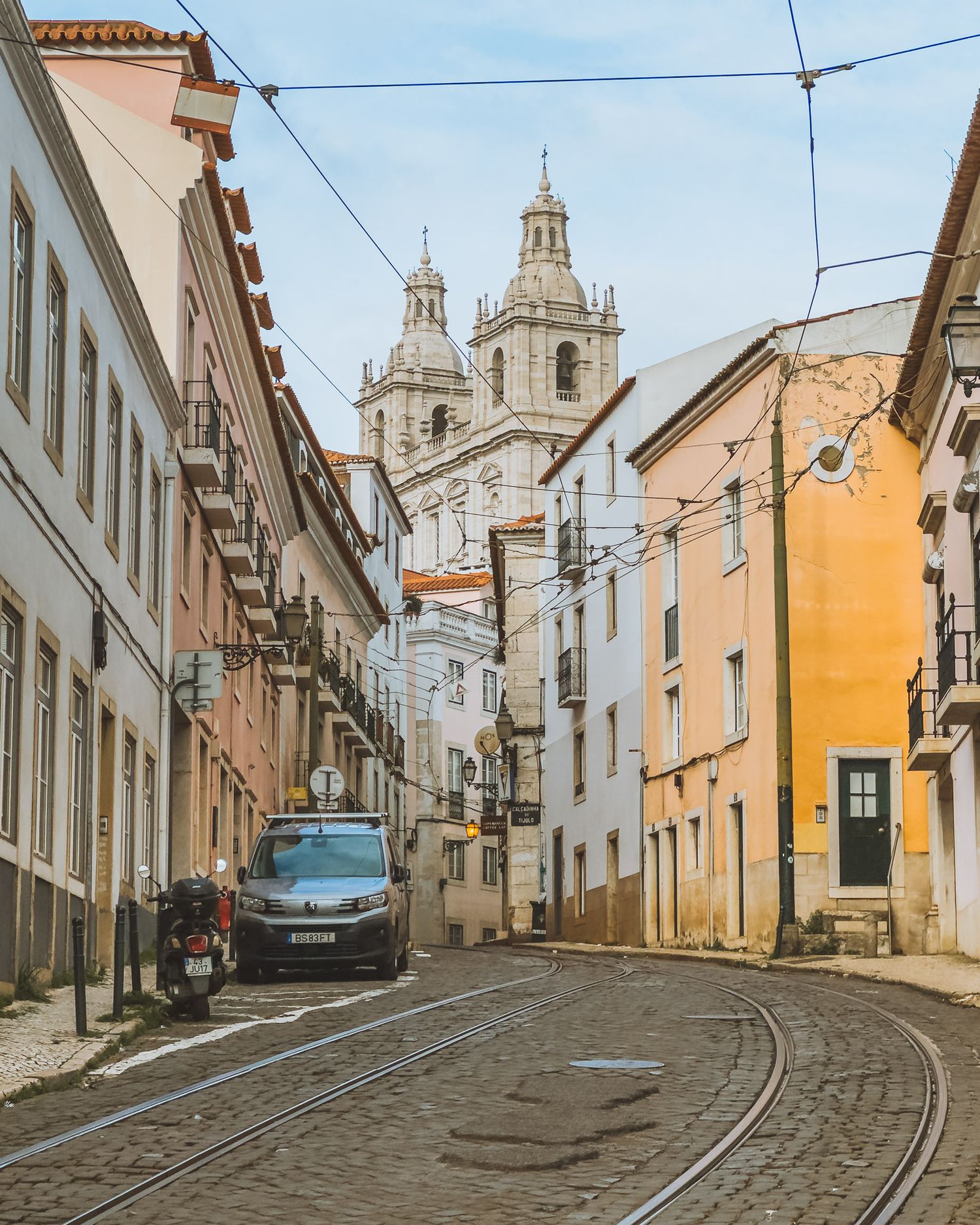 Historic church towers visible at end of narrow street lined with colorful buildings.