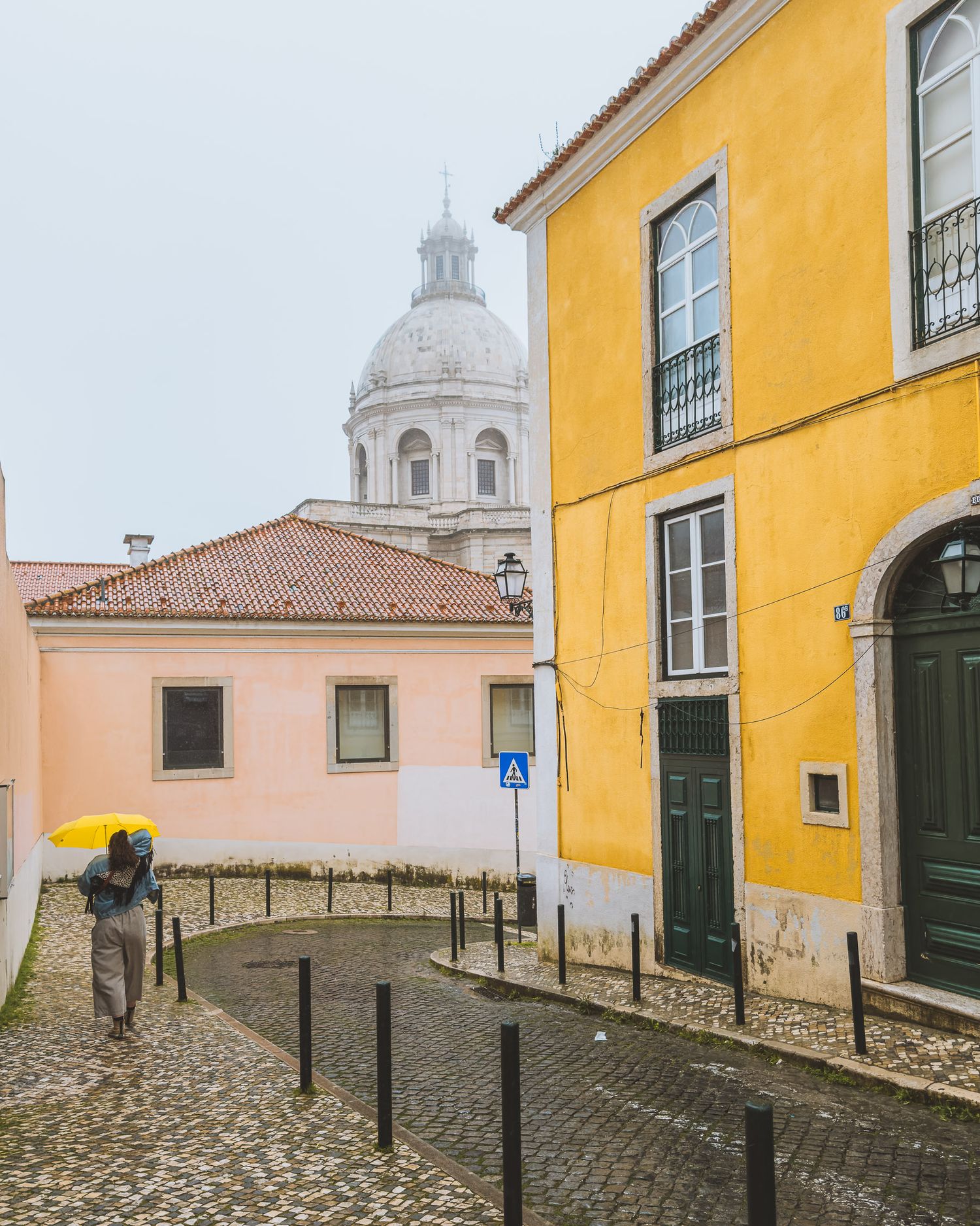 Cobblestone street with yellow buildings and white church dome in Lisbon, Portugal.