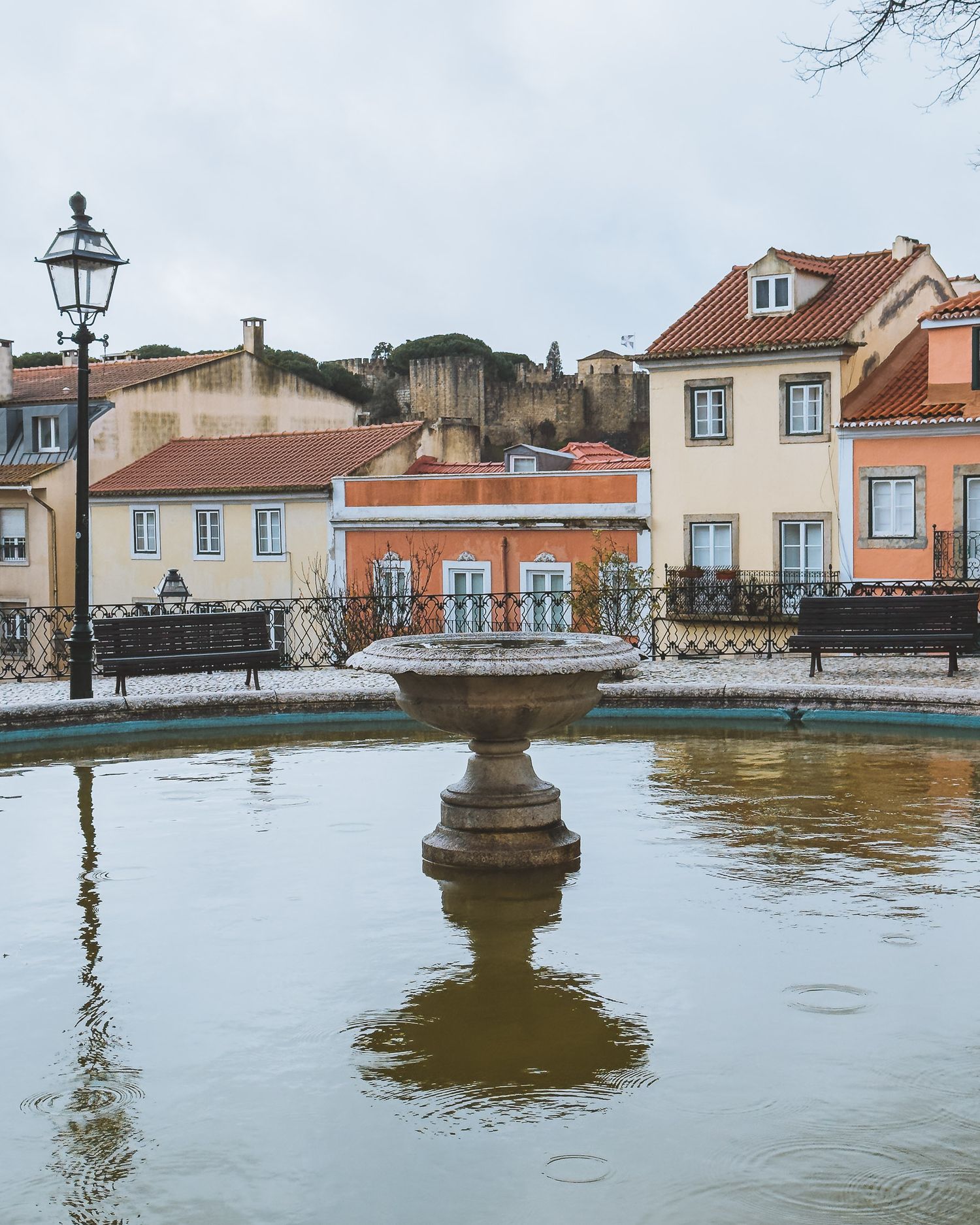 Panoramic view of waterfront buildings and lamp posts reflected in calm water.