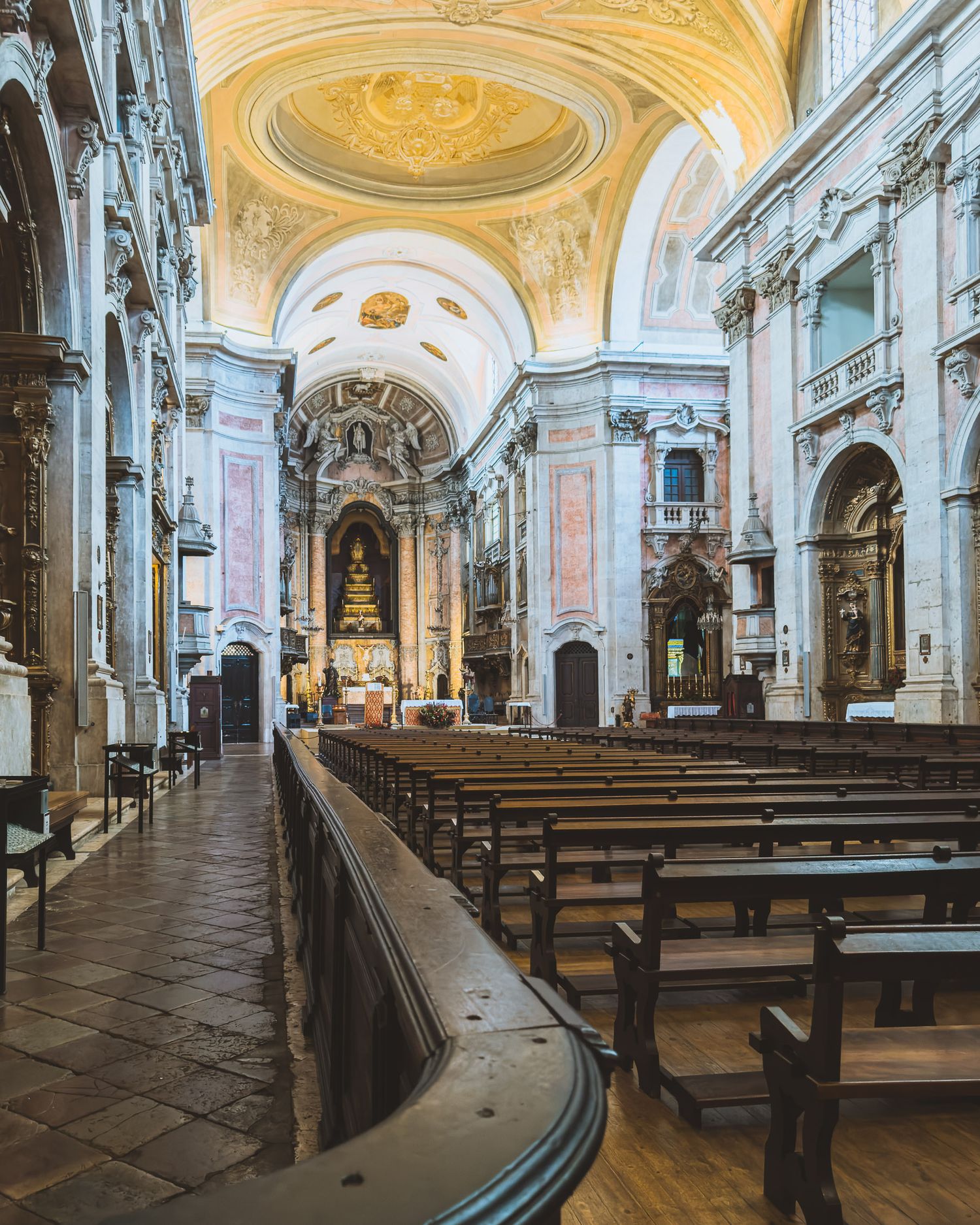 Interior of an ornate baroque church with wooden pews and vaulted ceiling decorated with gold details.