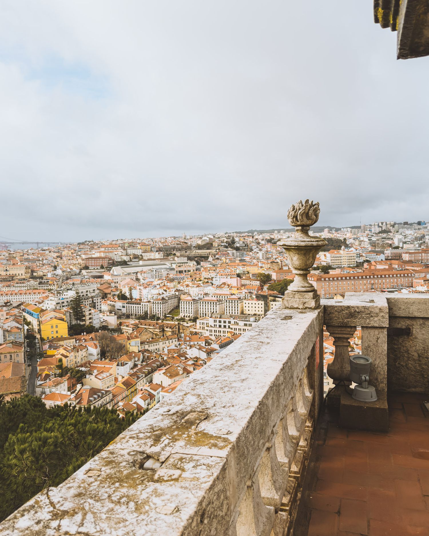 Panoramic cityscape view of Lisbon from an elevated terrace showing traditional red-tiled roofs.