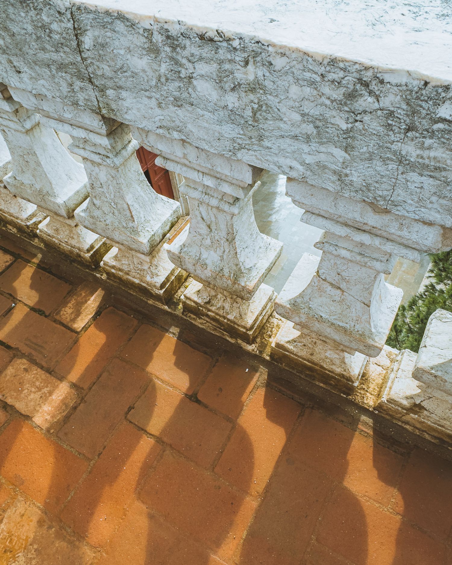 White stone balustrade casting dramatic shadows on terracotta colored floor.