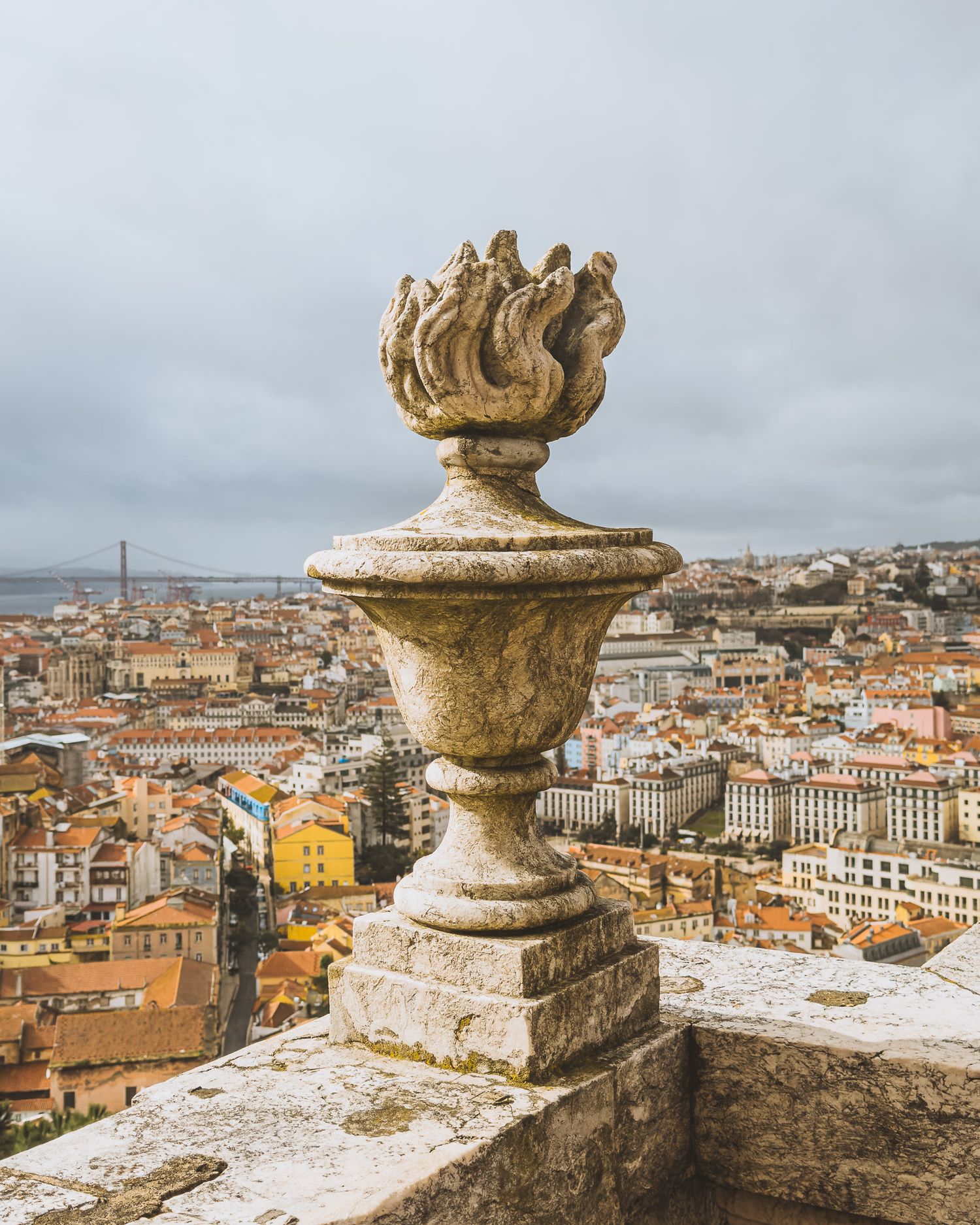 Panoramic view of Lisbon's cityscape with ornate stone finial in foreground.