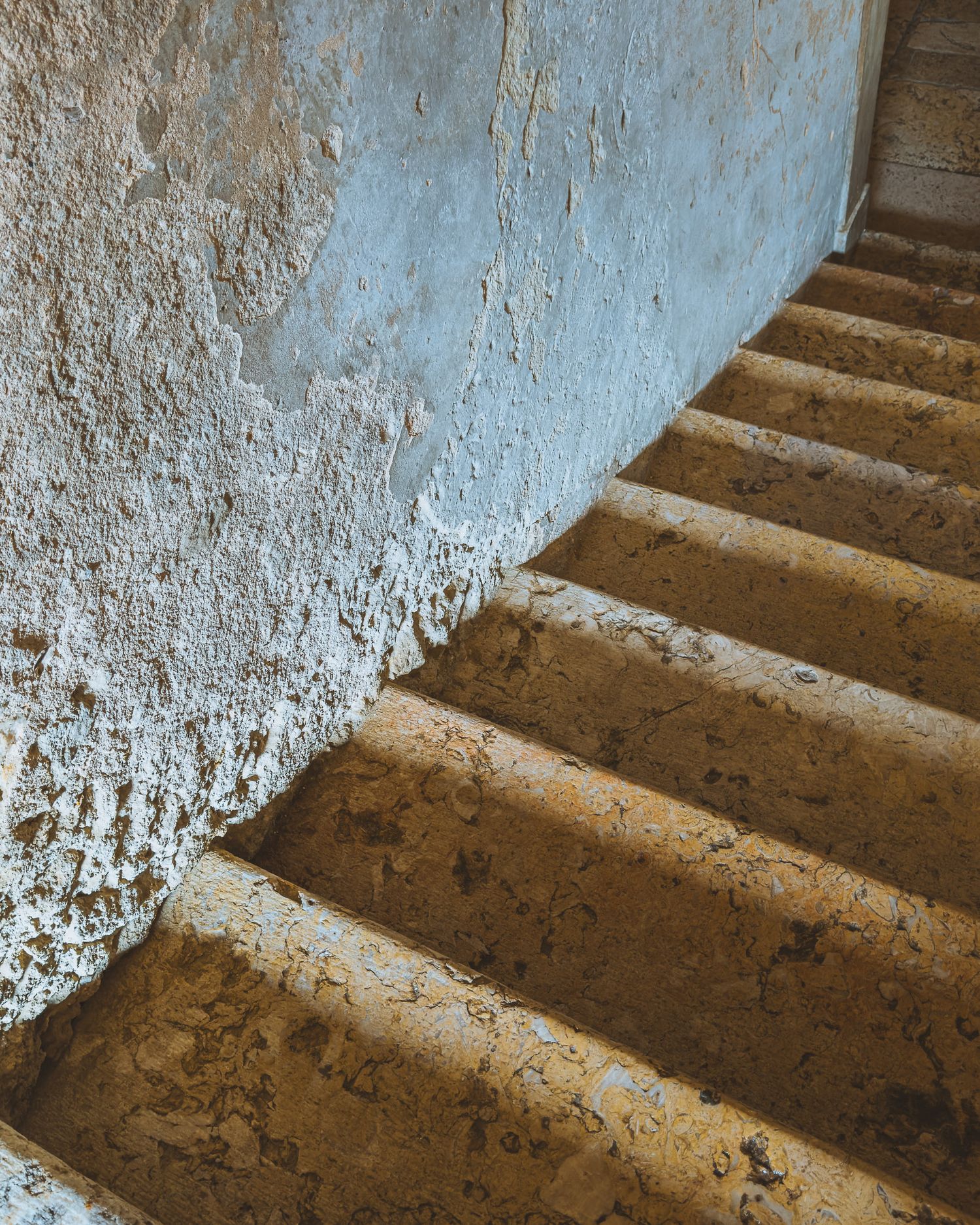 Ancient stone staircase with weathered white walls and dramatic shadows.