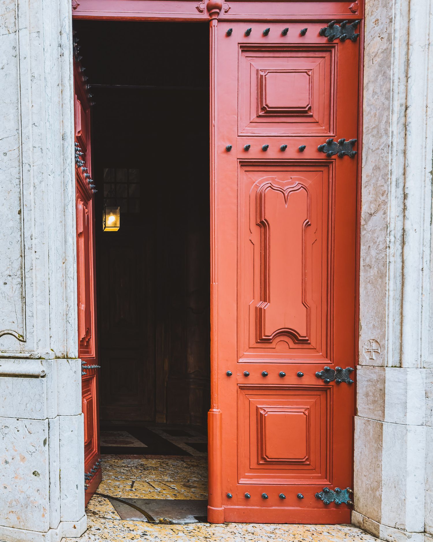 Large red wooden doors with decorative panels and iron hardware in a stone doorway.