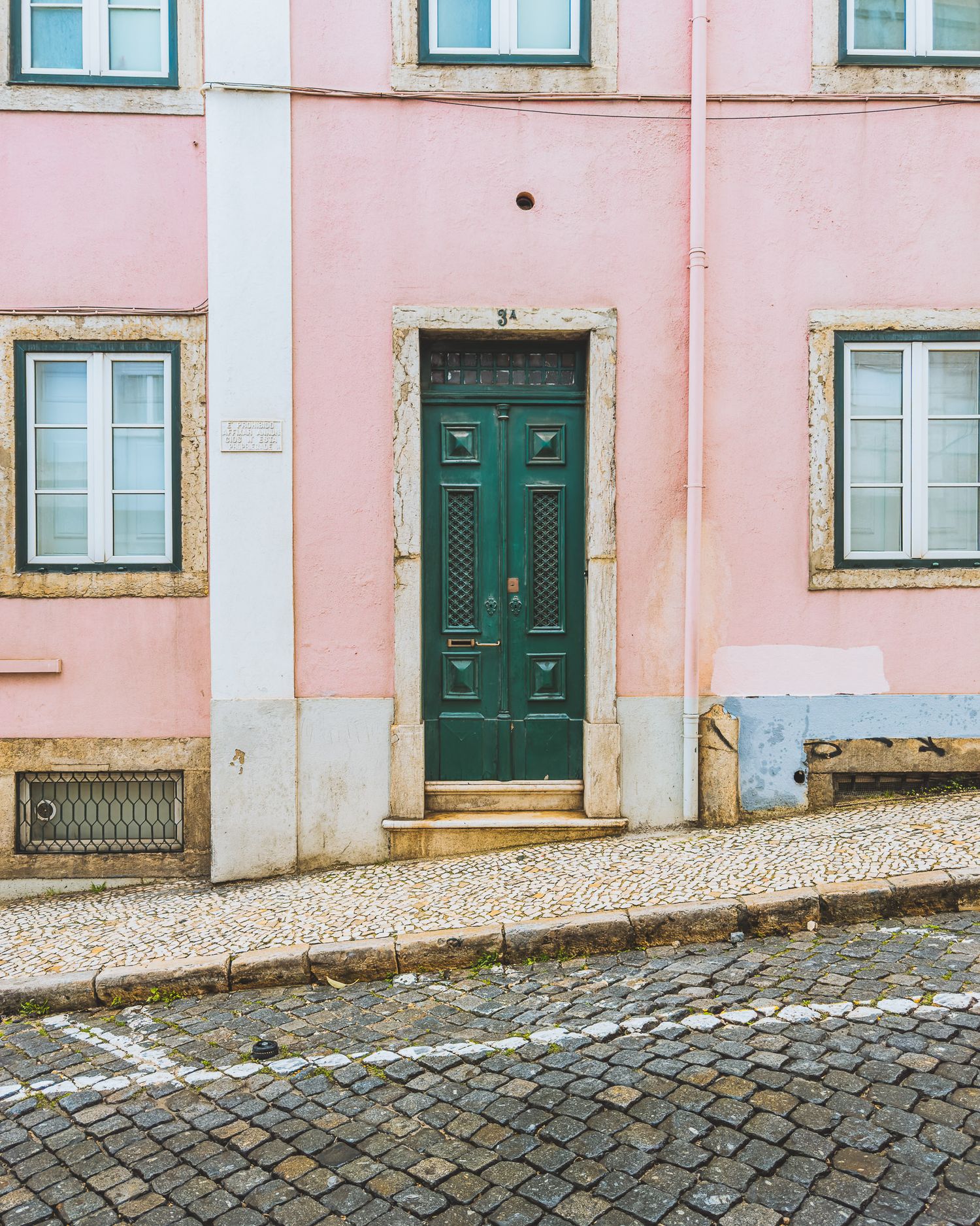 Pink building facade with green doors and windows on a cobblestone street in Portugal.