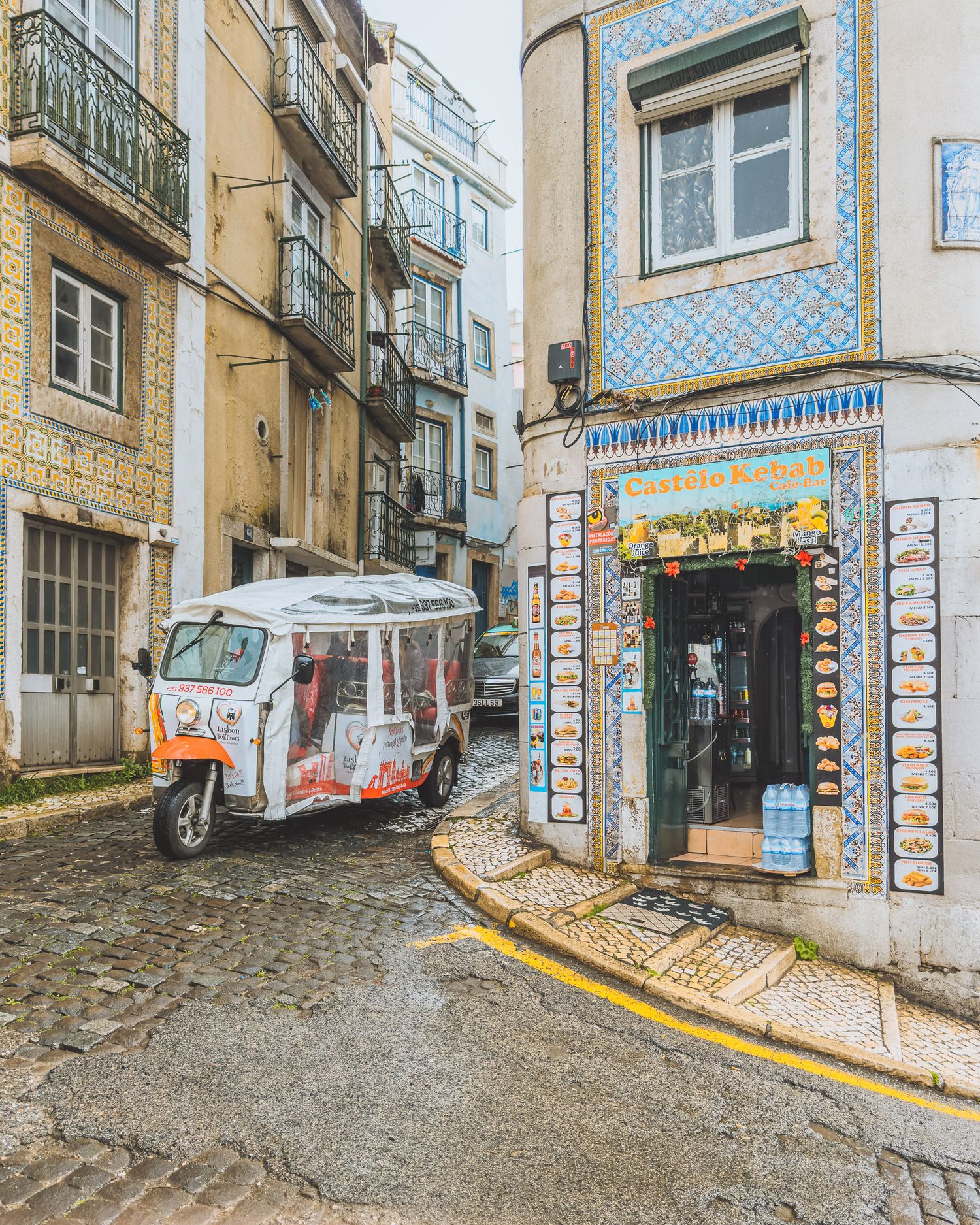 Narrow cobblestone street with traditional Portuguese tiled buildings and parked vehicles.