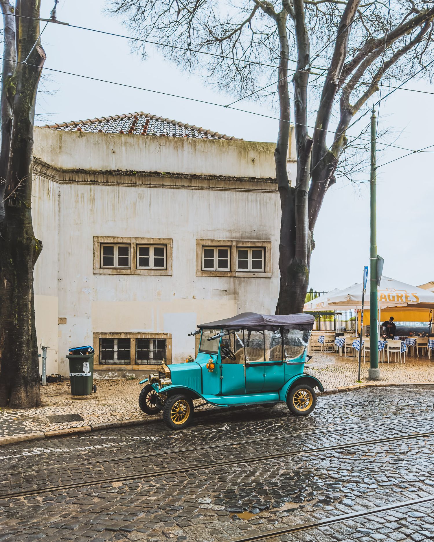 Vintage turquoise cars parked along a cobblestone street next to white buildings.