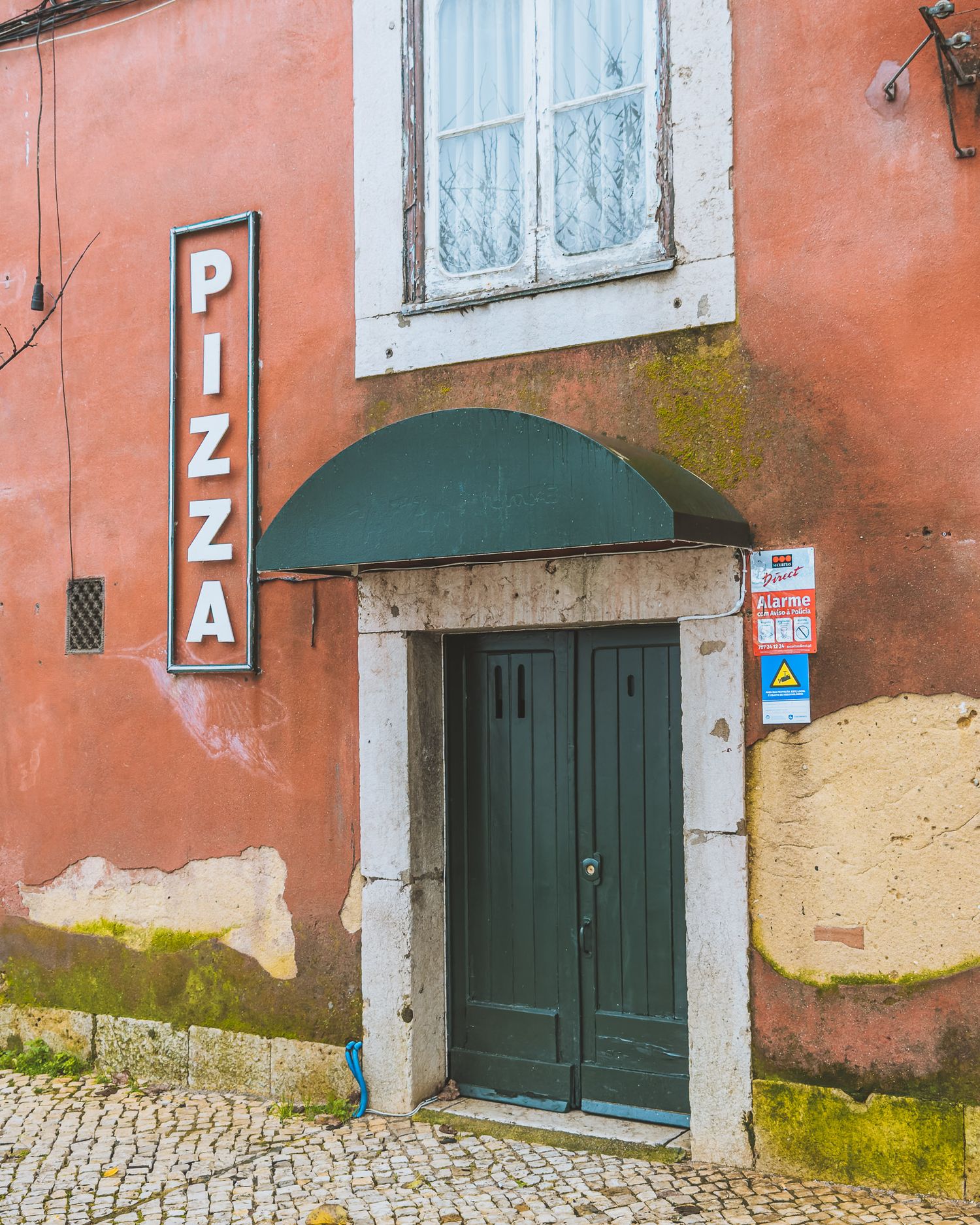 Weathered coral-colored building with green doors and white trim on a cobblestone street.