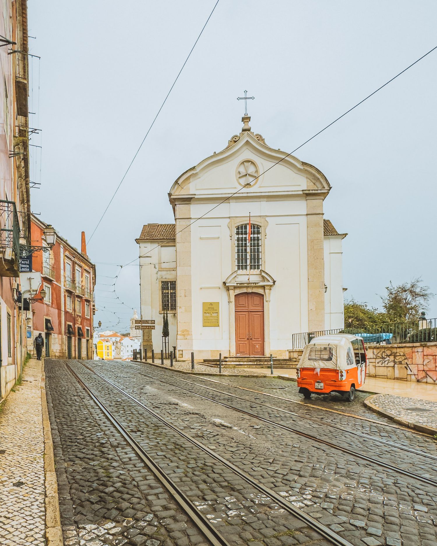 White church facade at the top of a steep cobblestone street with an orange tram visible.