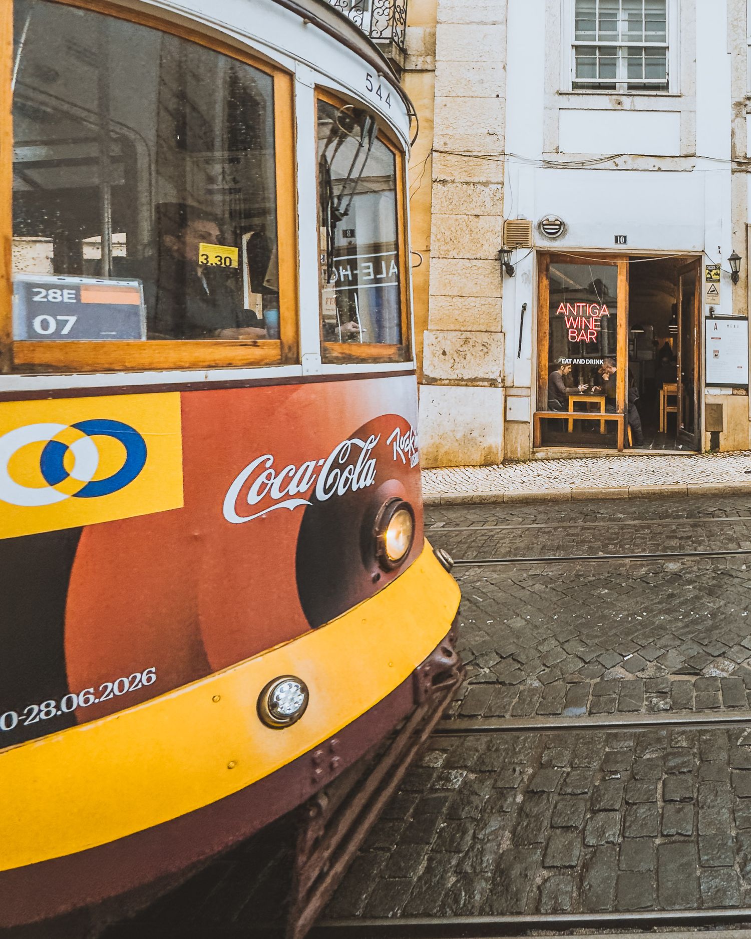 Yellow and orange vintage tram with Coca-Cola advertisement on cobblestone street.