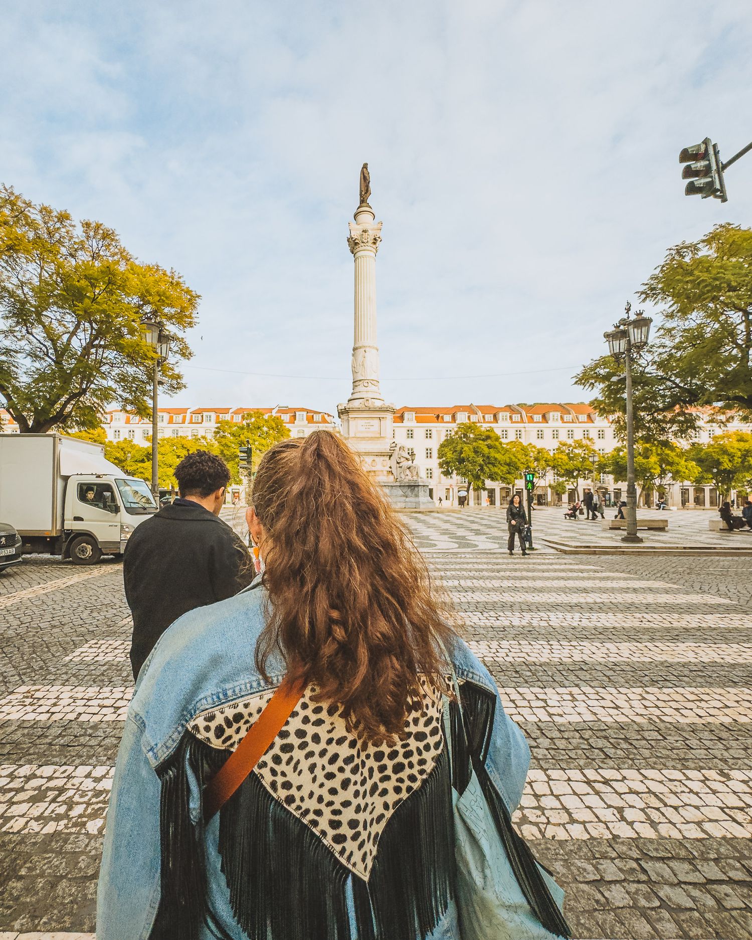 Wide cobblestone plaza with monument and historic buildings under cloudy skies in Lisbon.