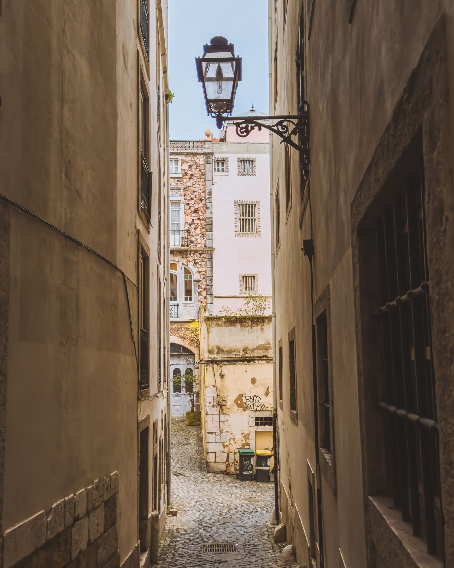 Narrow alley between old stone buildings leading to a church tower in historic Lisbon.