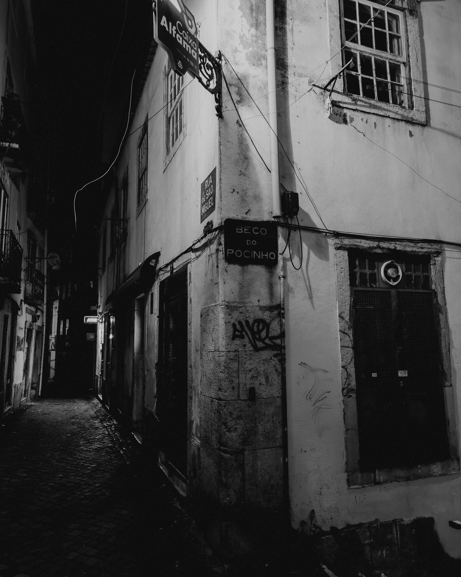 Dark narrow alley with old buildings and graffiti in black and white photography.
