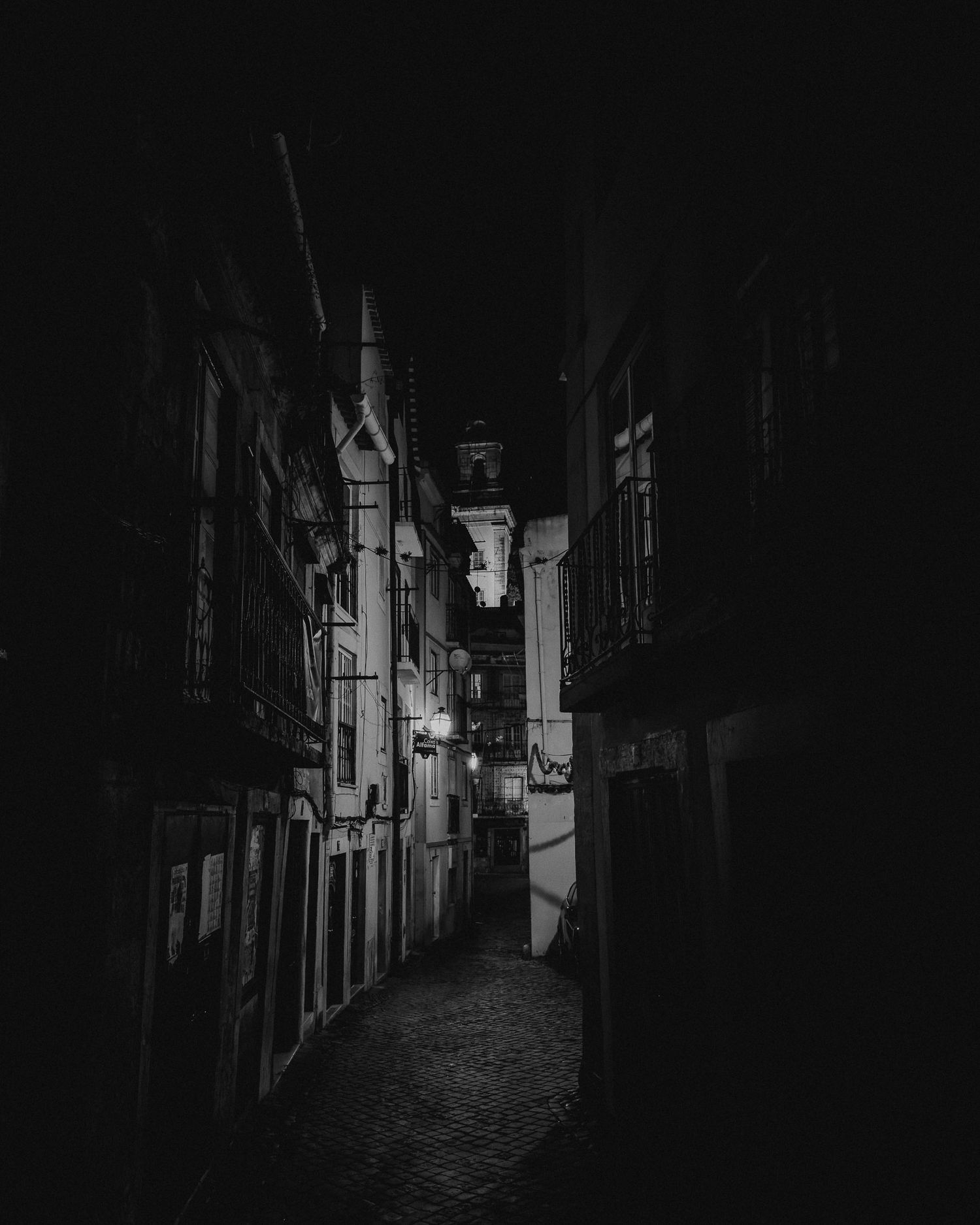 Moody black and white photograph of a narrow European alleyway at night.