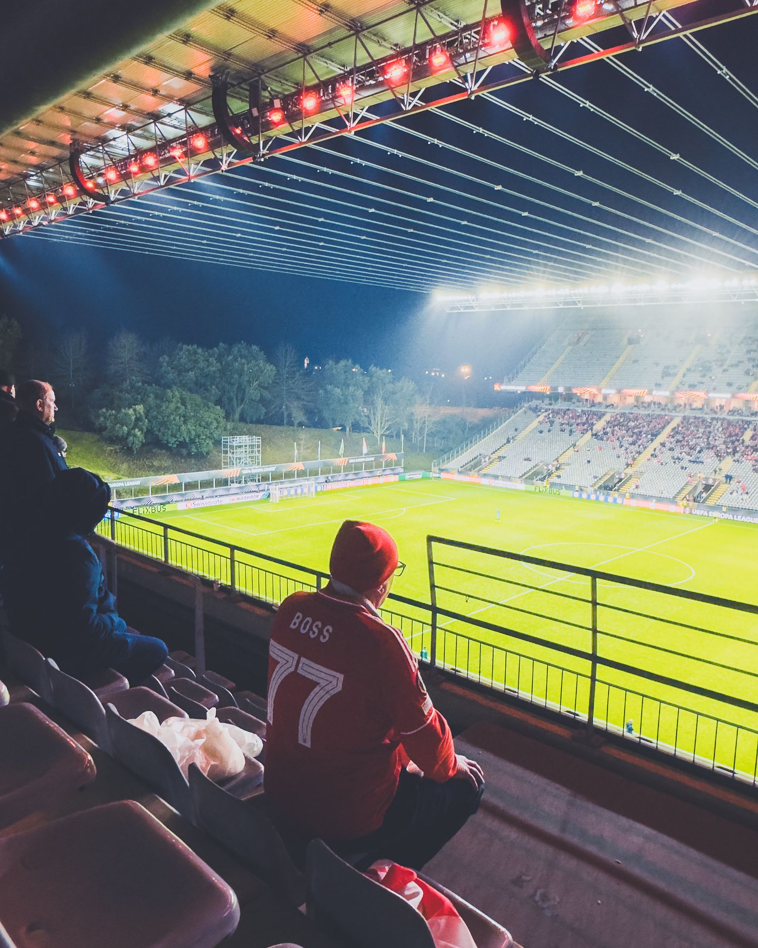 View of illuminated soccer stadium from upper stands with spectators watching the game.