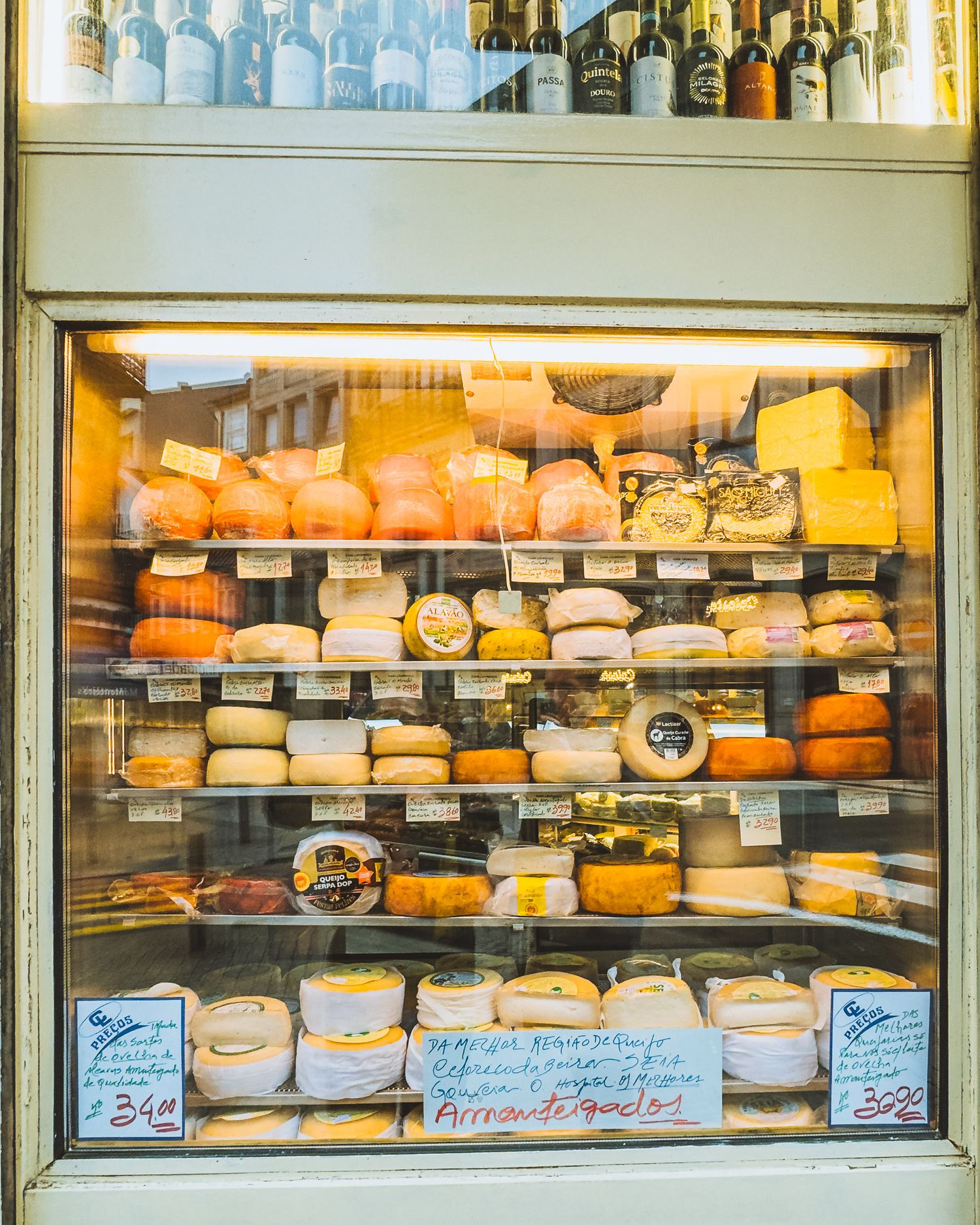 Display case filled with various gourmet cheeses and bottles in a shop window.