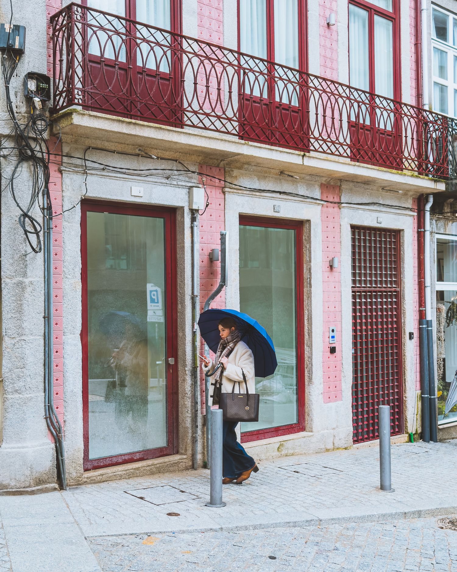 Historic storefront with pink walls and ornate red metalwork balconies along a cobblestone street.