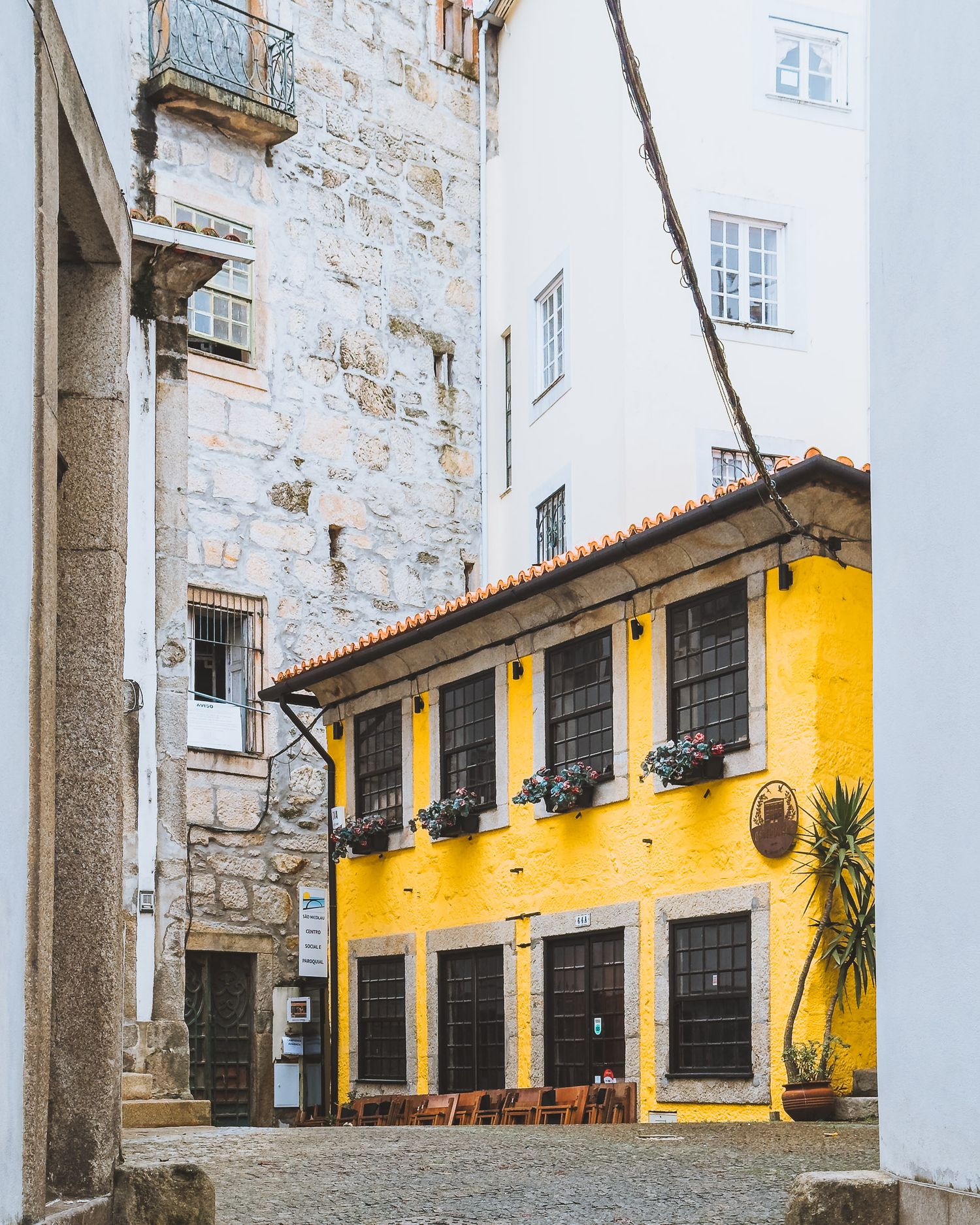 Yellow building with black shuttered windows and stone walls in a historic courtyard setting.