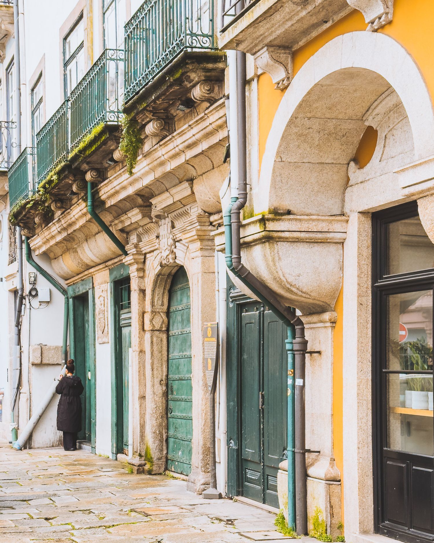Traditional European street architecture with yellow walls, green shutters and ornate stone arches.