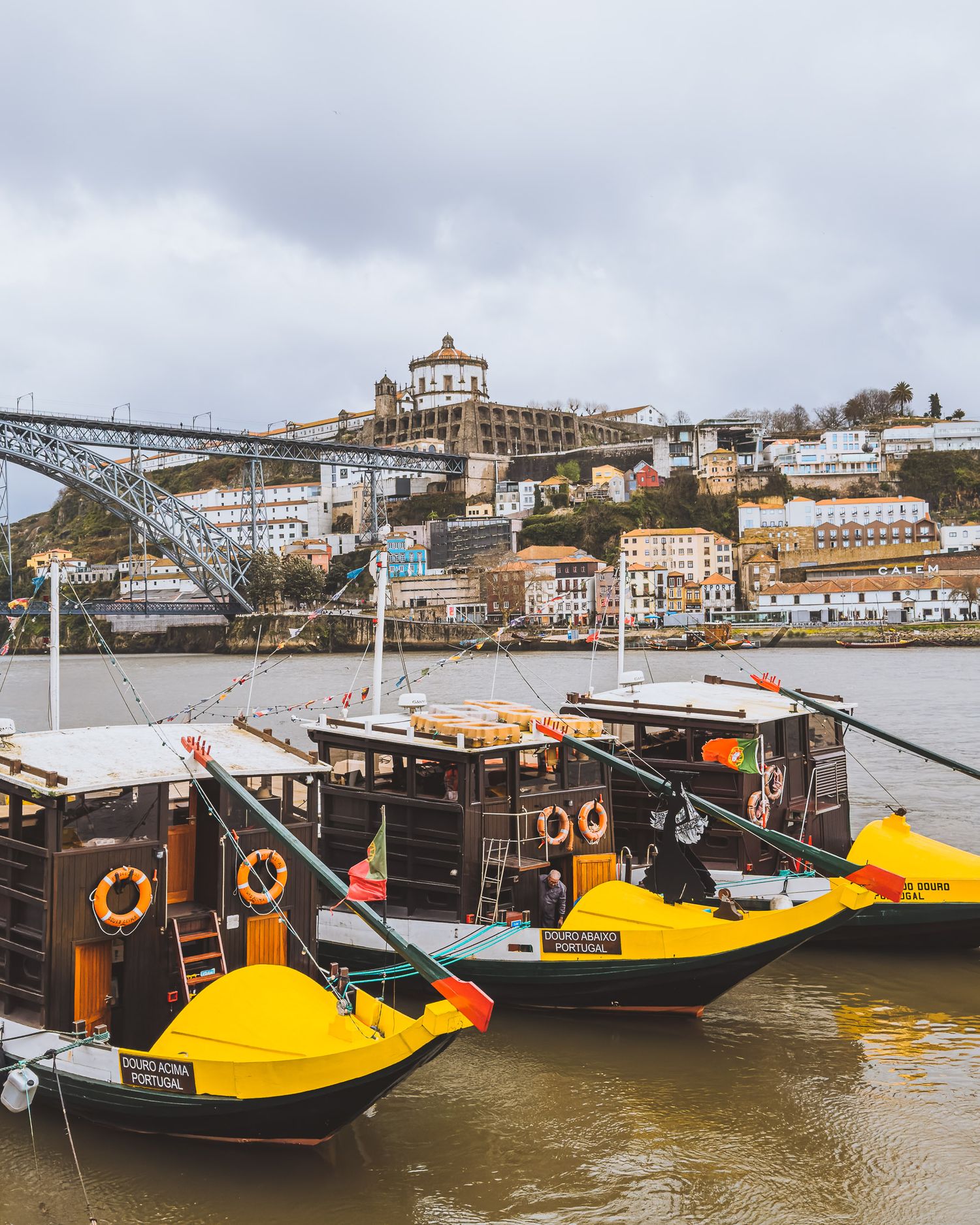 Traditional Portuguese rabelo boats with yellow and black hulls docked along a riverfront.