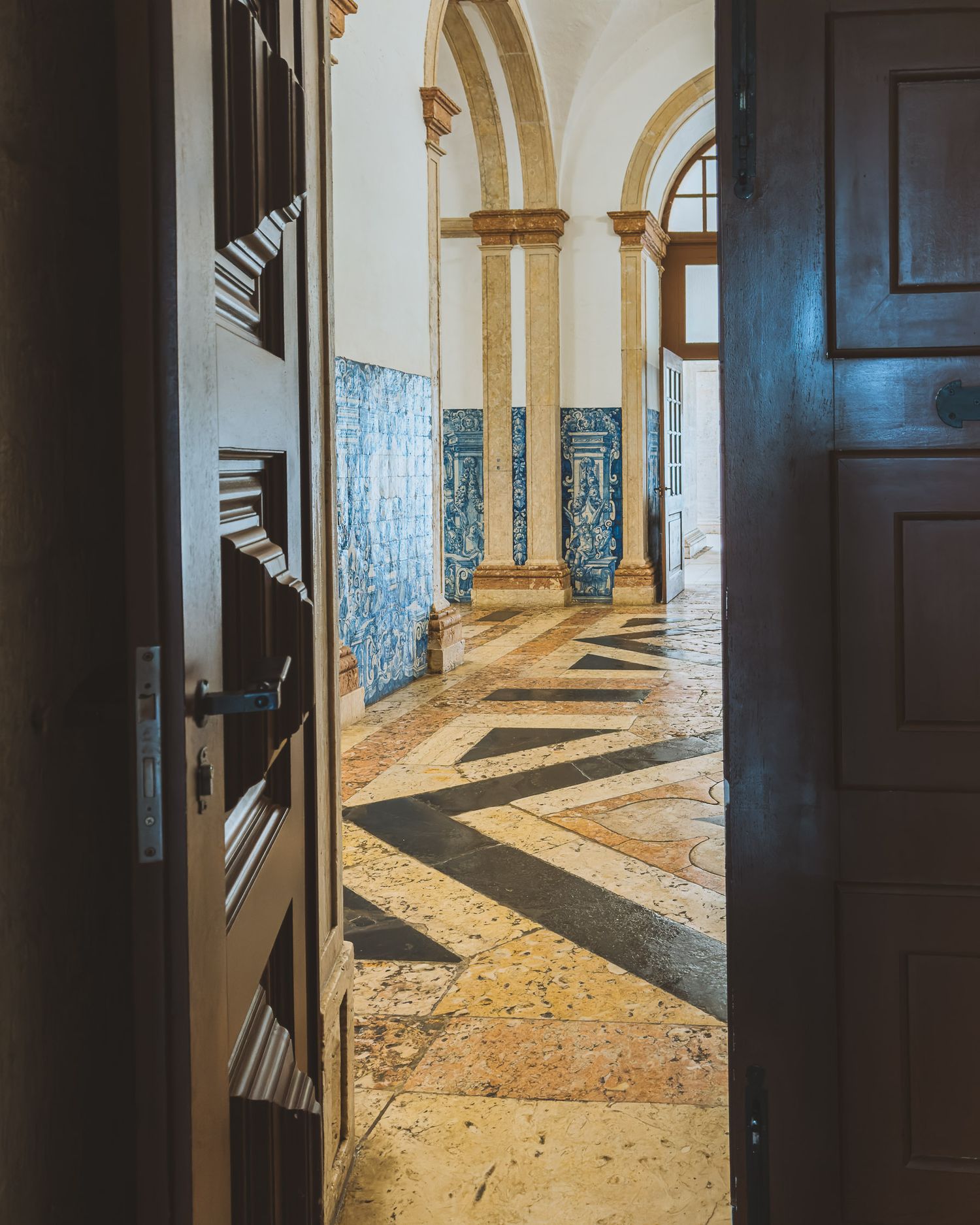Sunlit corridor with arched columns and tiled walls casting dramatic shadows.