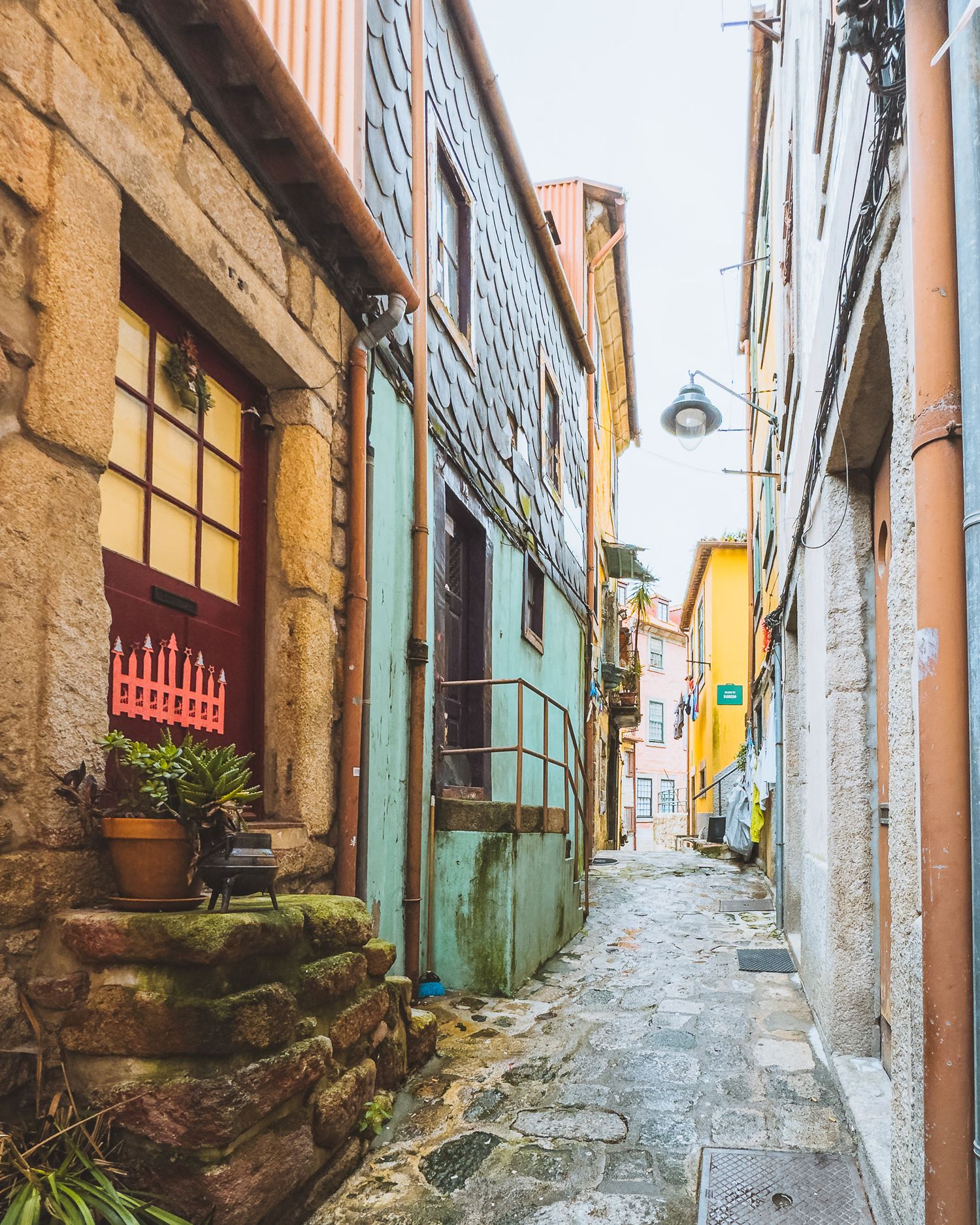 Steep cobblestone alley between old stone buildings with potted plants and colorful walls.