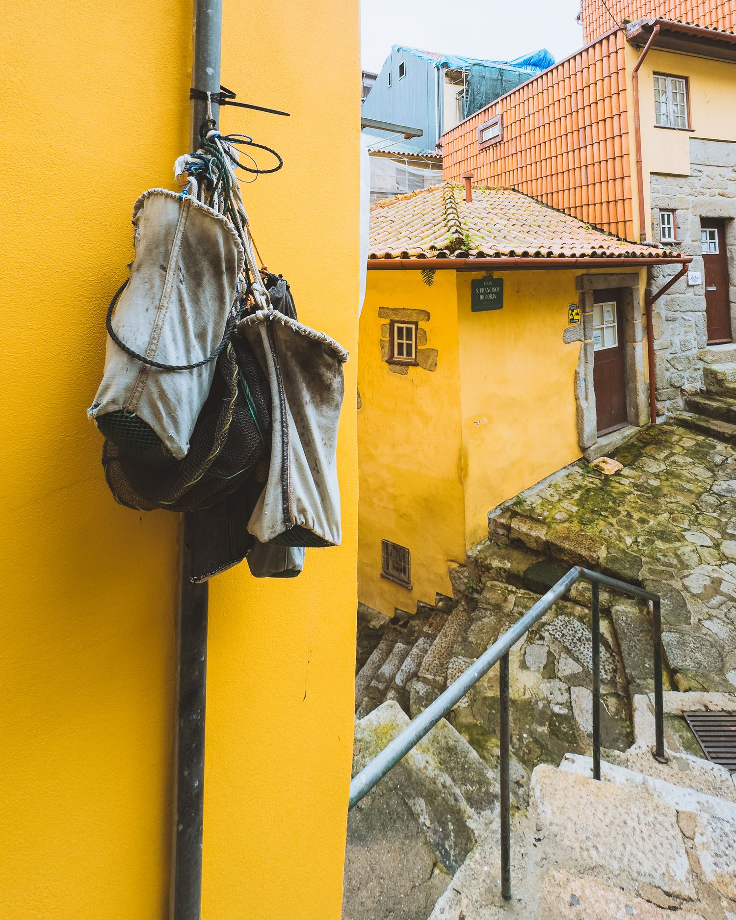 Bronze statue mounted on yellow wall against terracotta rooftops in historic setting.