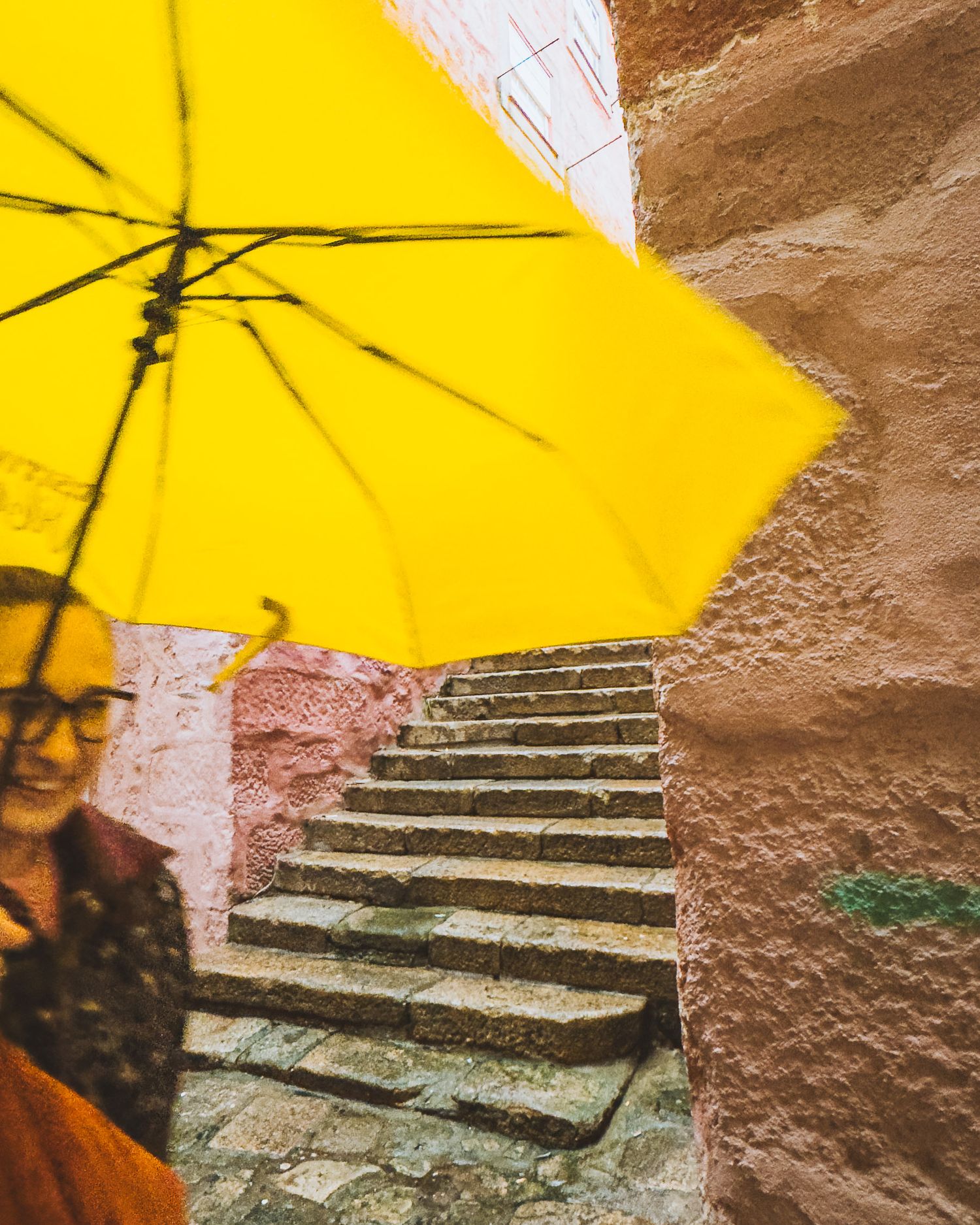 Stone steps with a bright yellow umbrella casting shadows in an old alley.