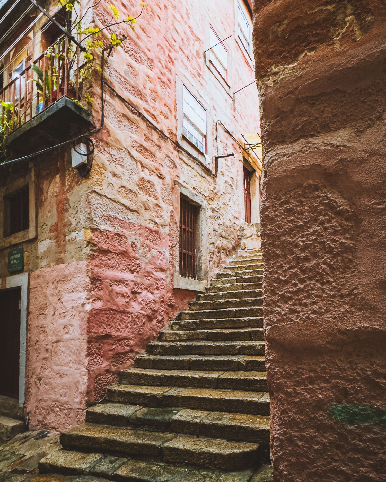 Pink-tinted stone stairway winding through a narrow medieval passageway. Porto.