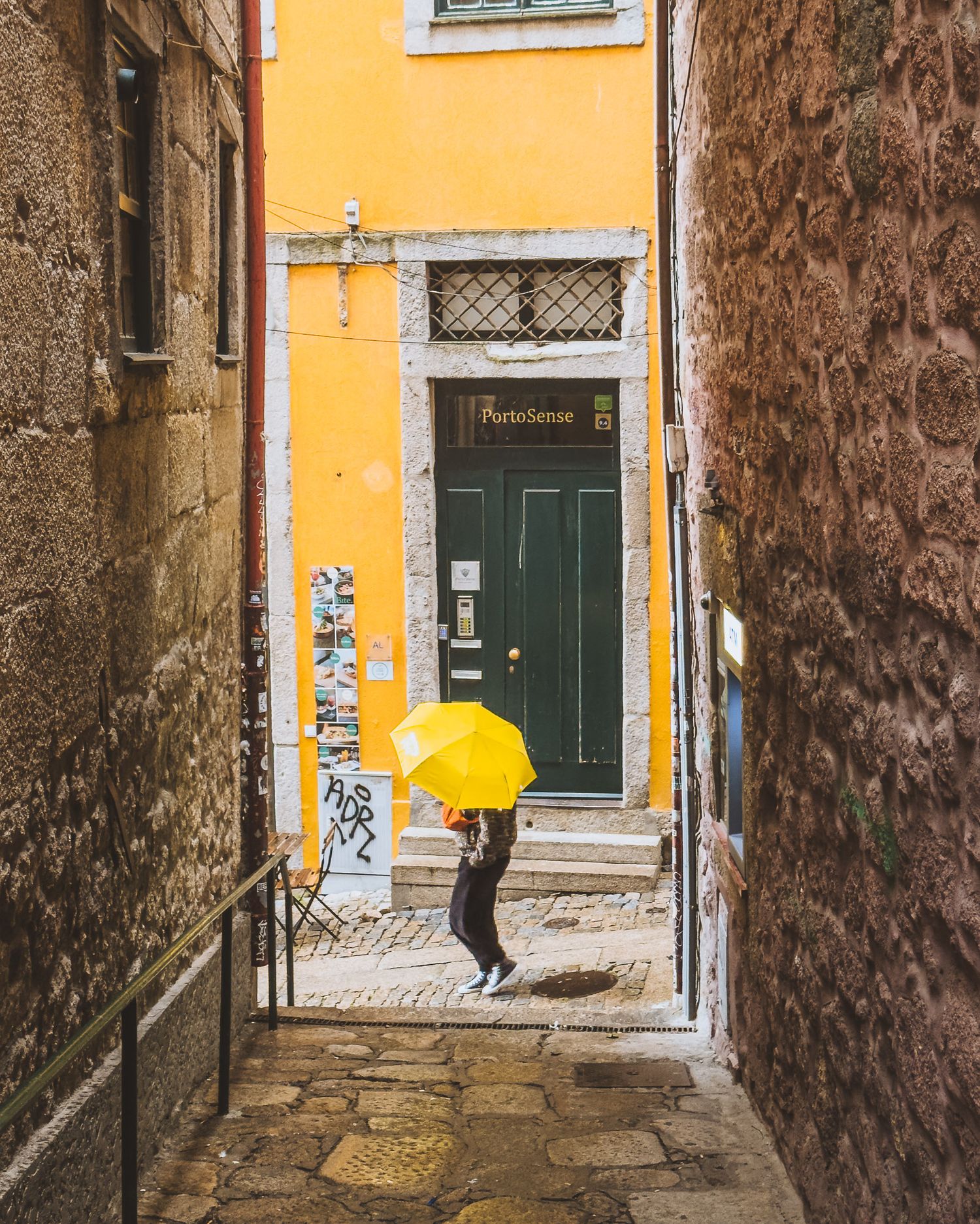 Narrow alley with bright yellow wall and green doors in an old European neighborhood. Porto.