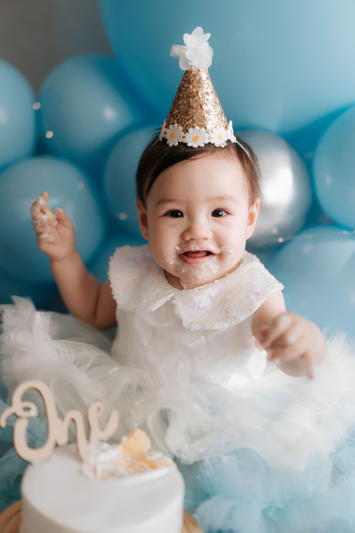 Happy baby wearing knitted bunny hat and romper sits on floor with smashed cake during first birthday photo shoot.