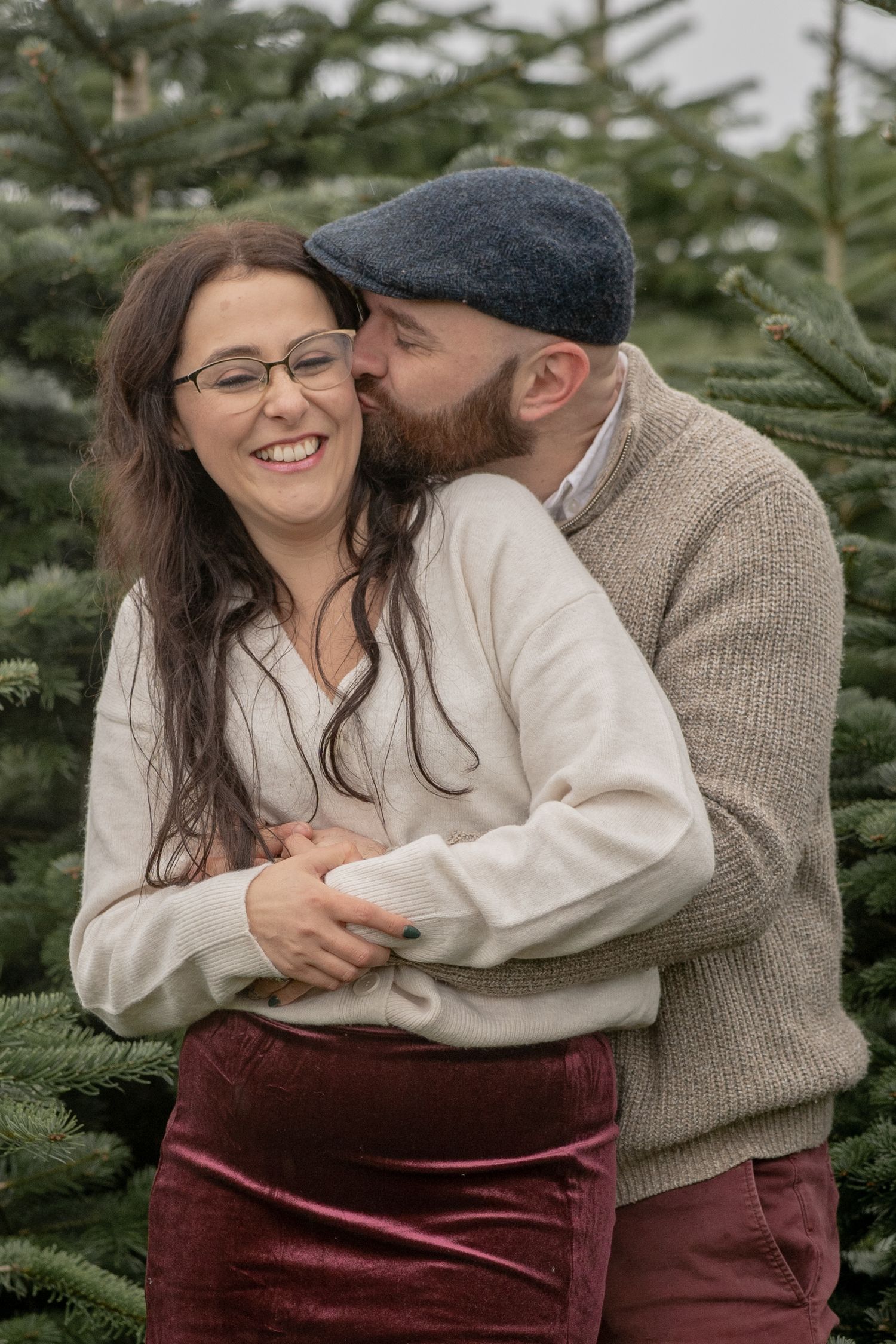 A couple embraces in a field while wearing a yellow sweater and green jacket on an overcast autumn day.